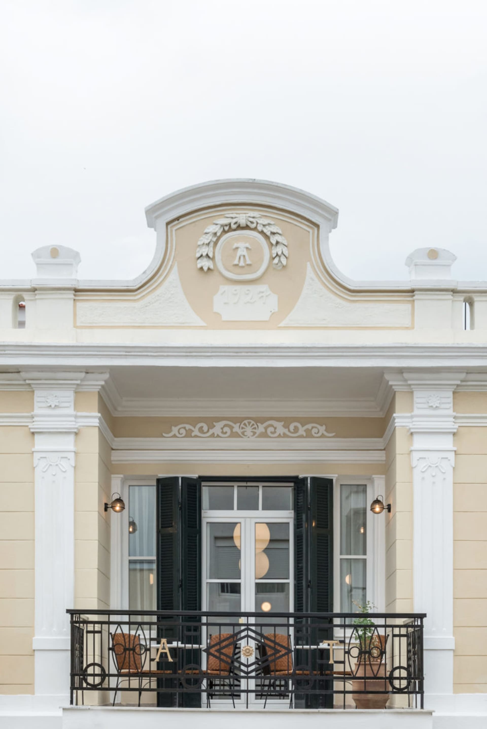 Facade of a building with concrete walls, black shutters, and an ornate logo above the door.