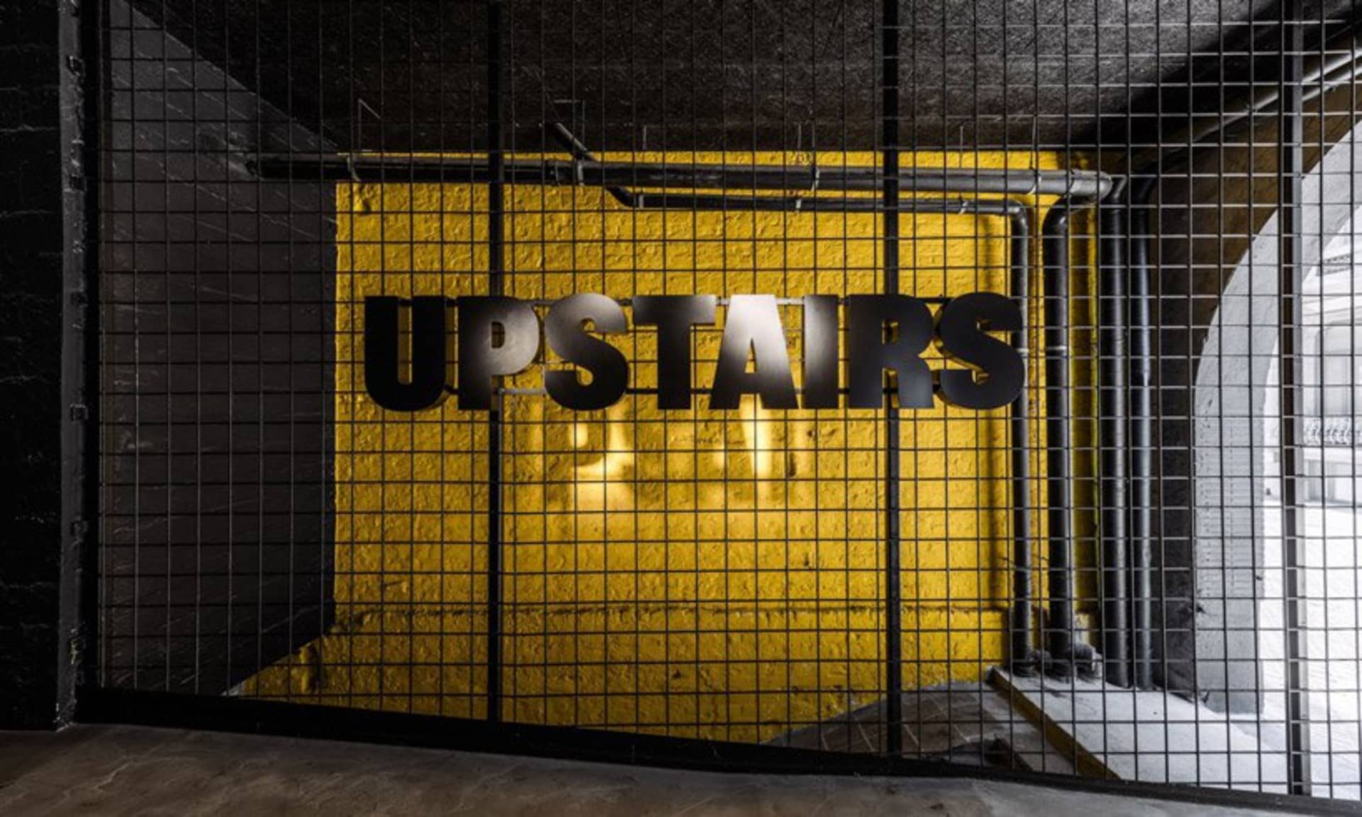Industrial sign that says 'UPSTAIRS' mounted on yellow tiled wall in an industrial-style interior