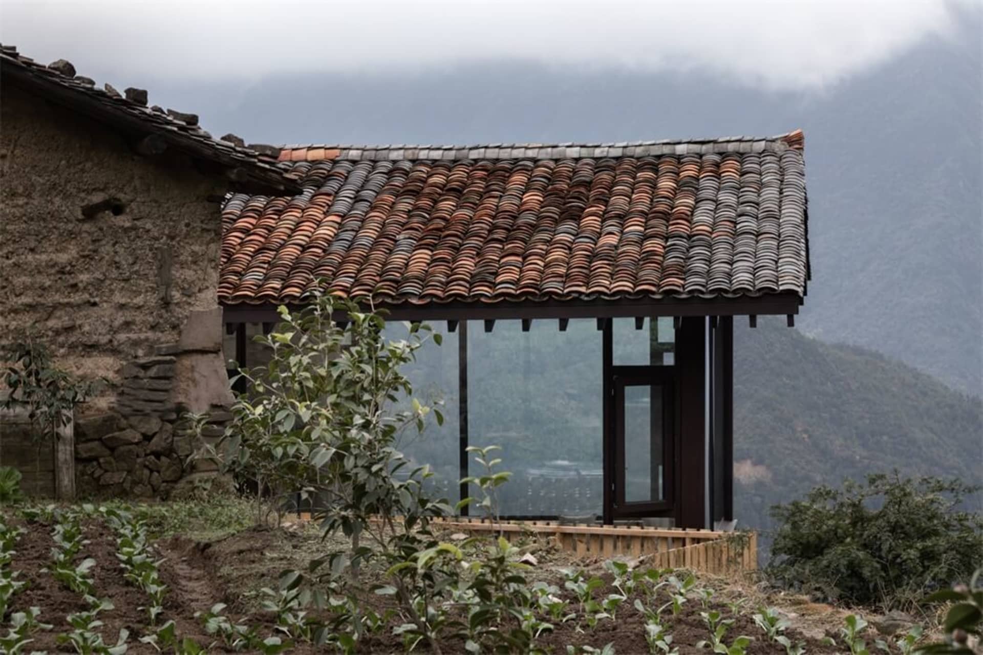 A traditional residence with a terracotta tiled roof and glass entrance, set against a mountainous backdrop.