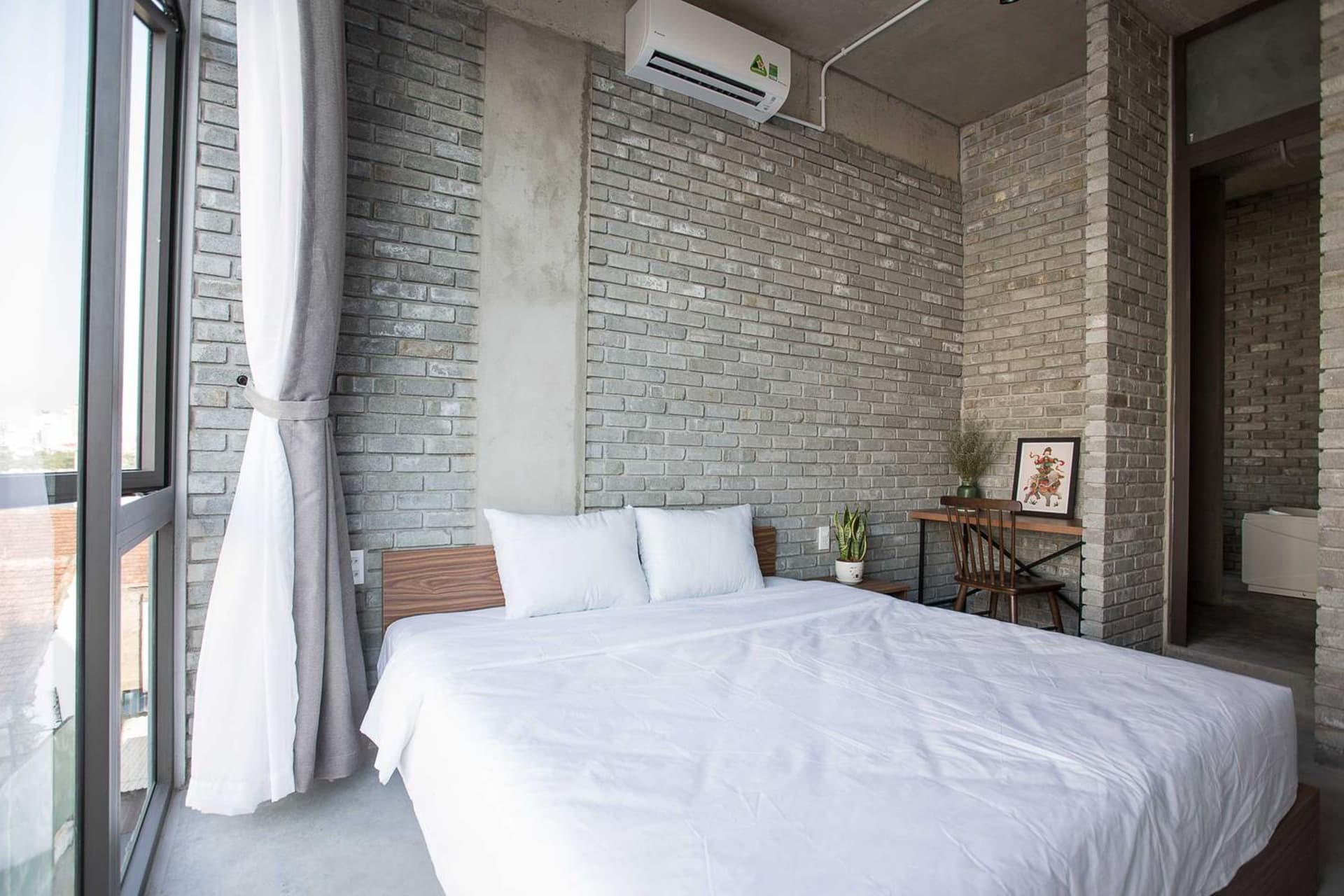 Modern bedroom with exposed brick walls, white bedding, and a large window