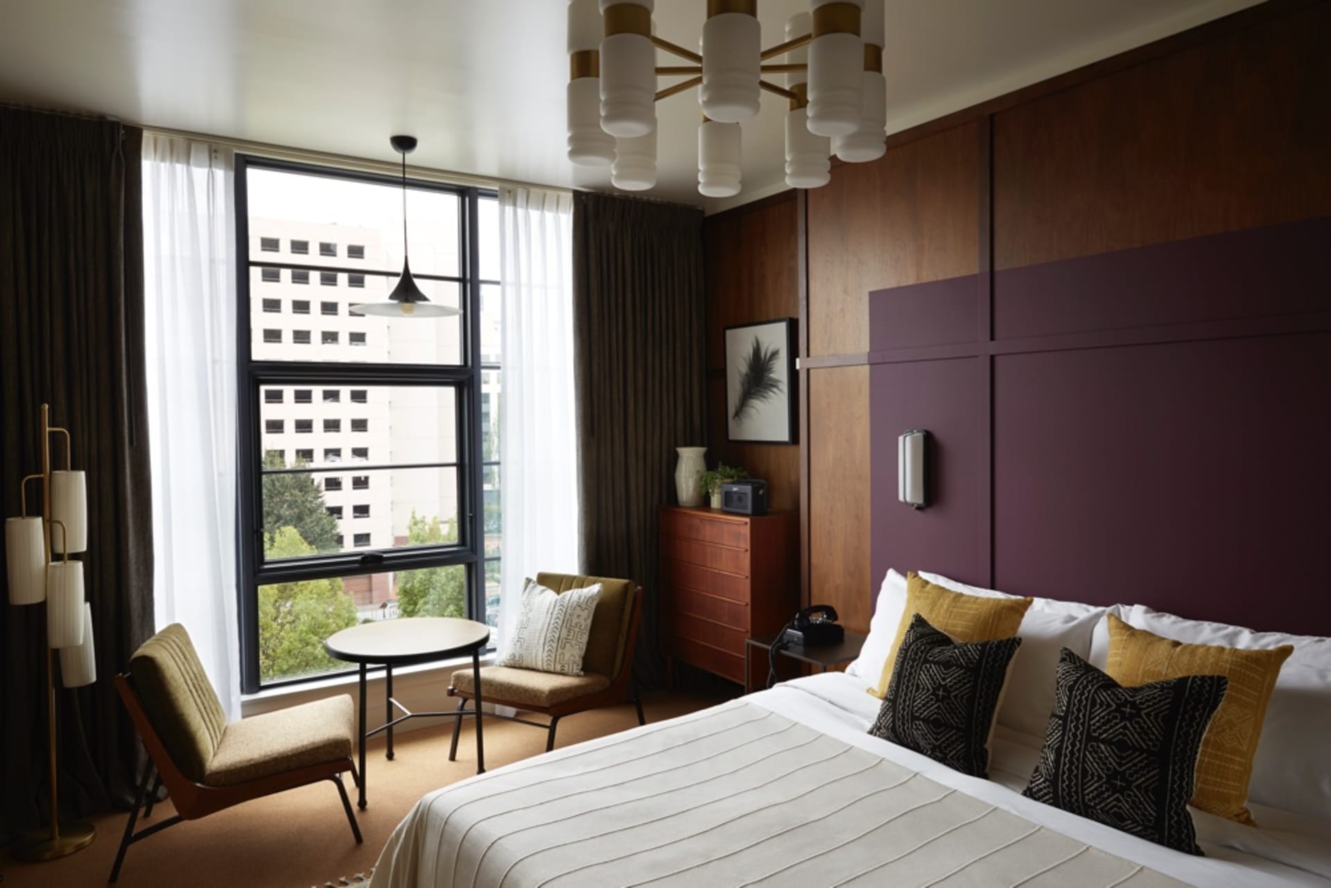 A modern hotel room featuring wooden paneling, fabric bedding, and metal accents.