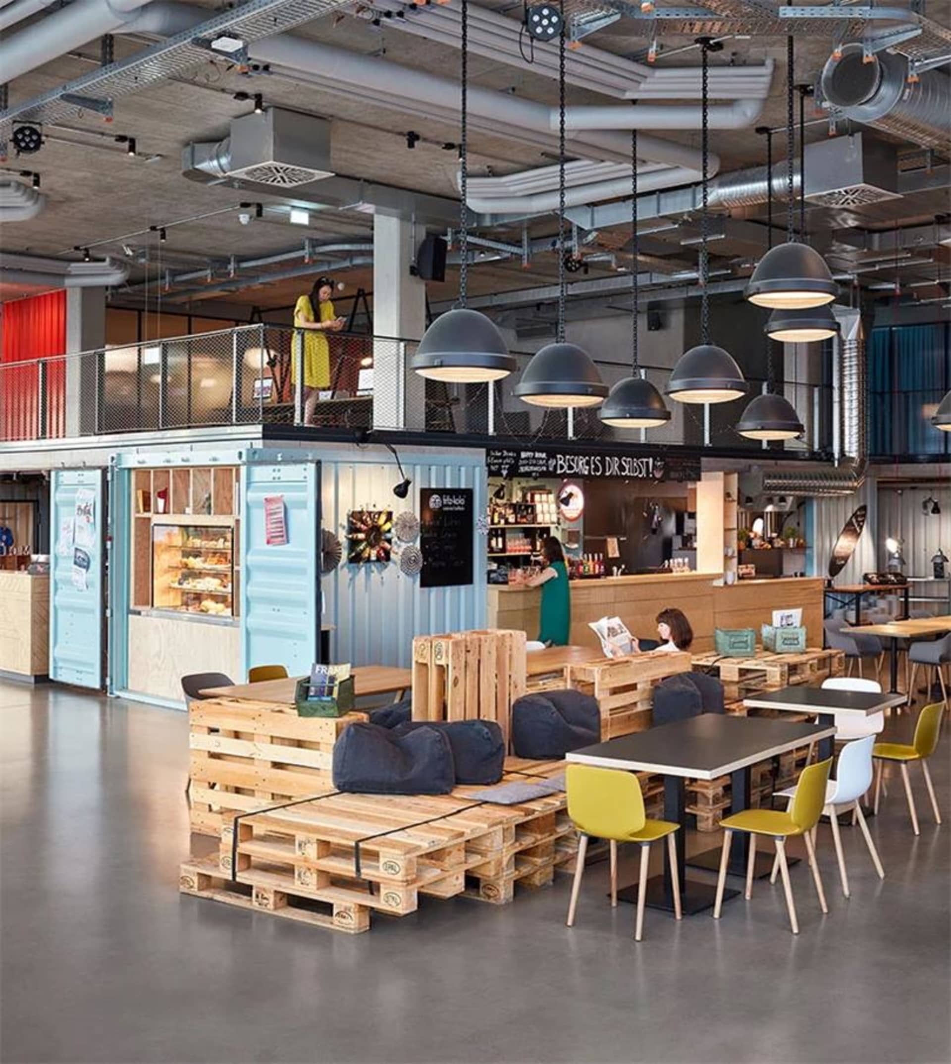 Modern industrial cafe lounge with pallet furniture, steel fixtures, and hanging lamps.