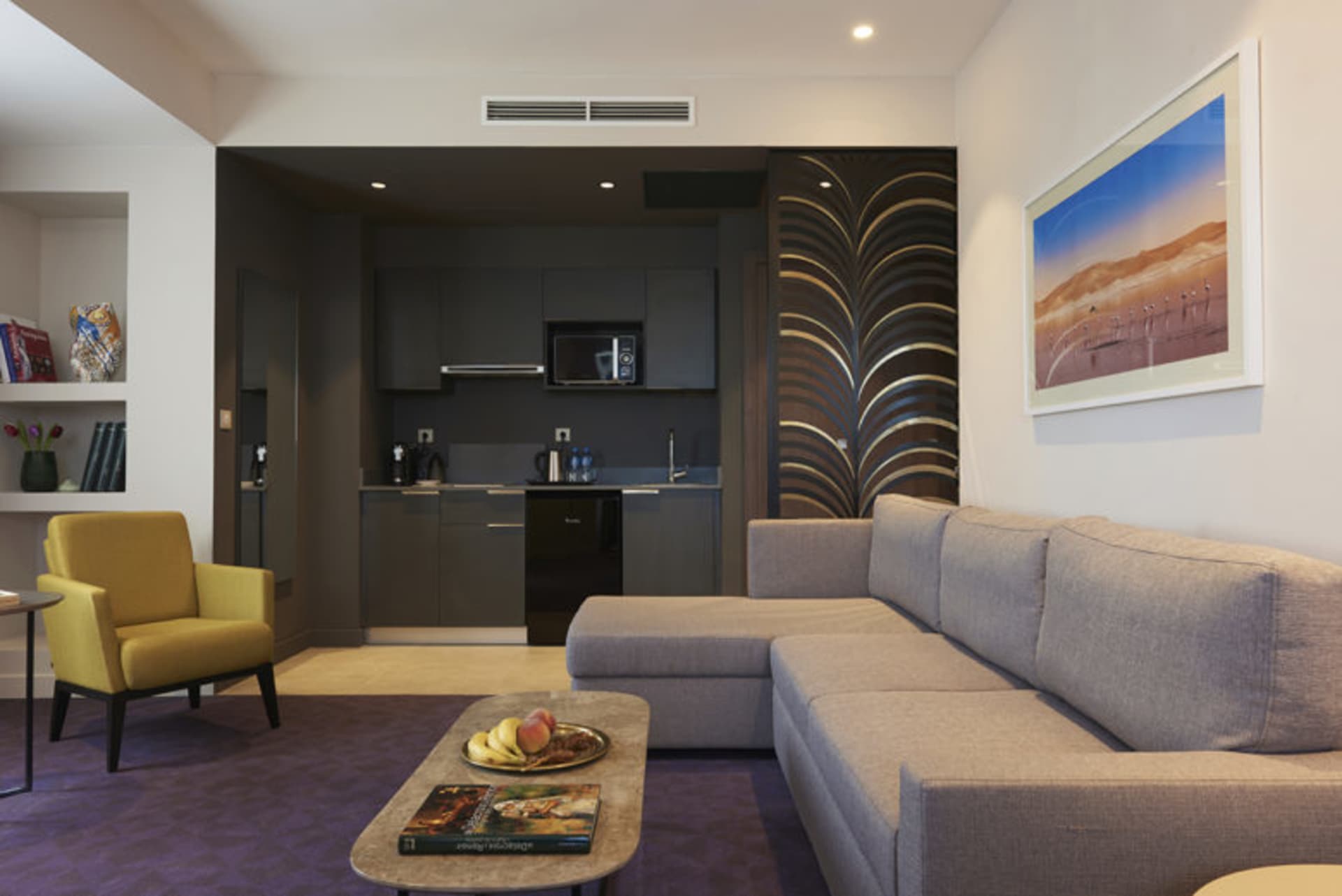 A modern living room with a grey fabric sectional sofa, a yellow upholstered armchair, a coffee table with a fruit bowl and a