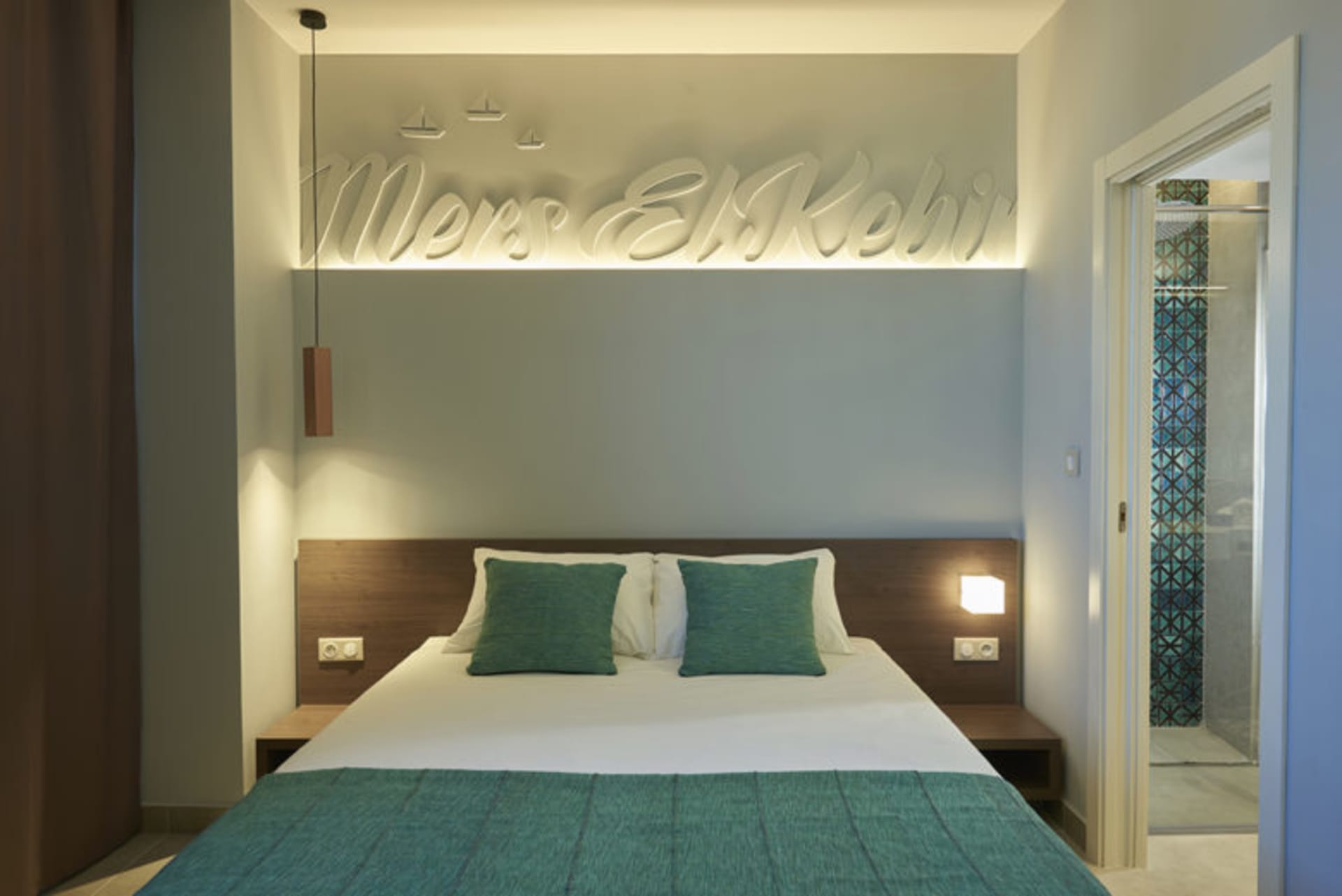 Modern minimalist bedroom with turquoise bedding, white walls, and wooden headboard.