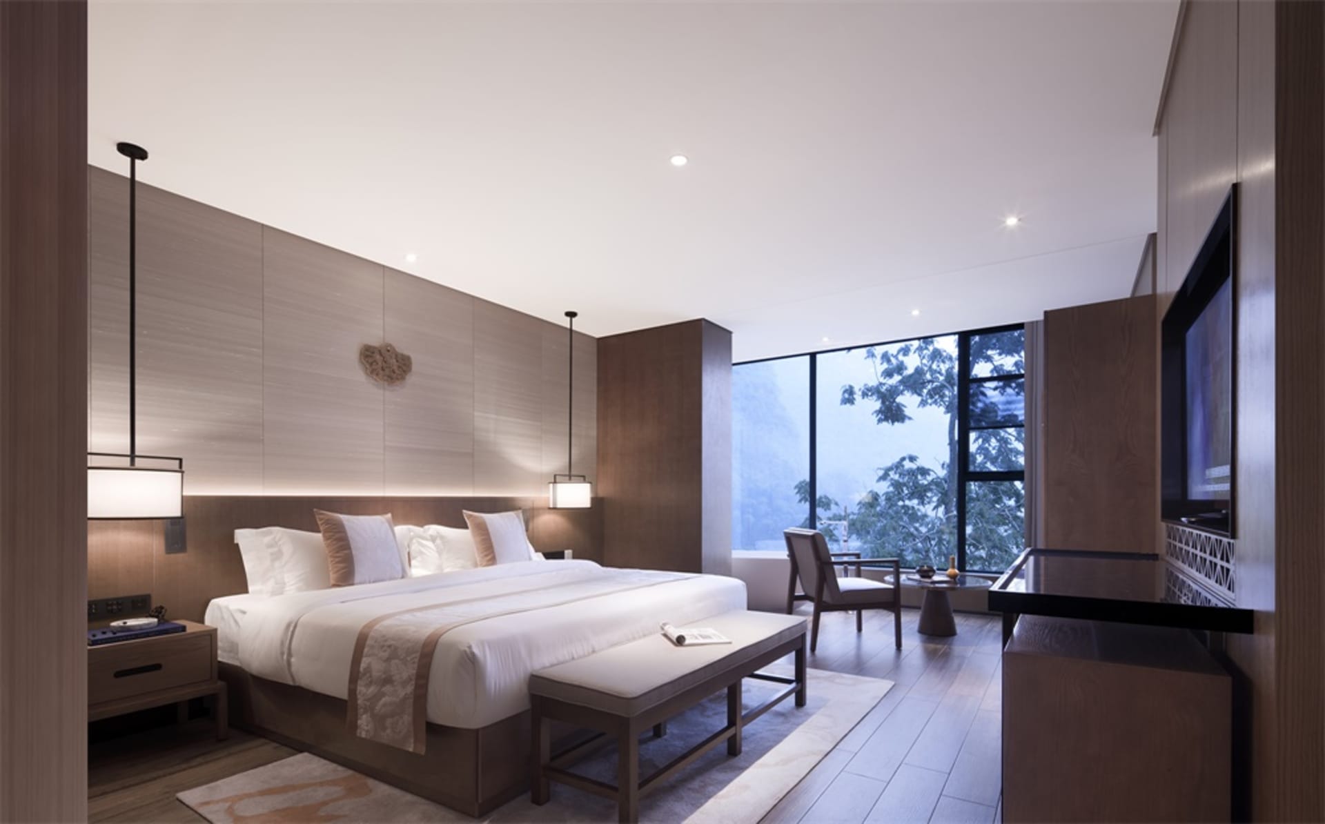 Modern minimalist bedroom featuring a large bed with white bedding, wooden furniture, and a large window with a view of trees