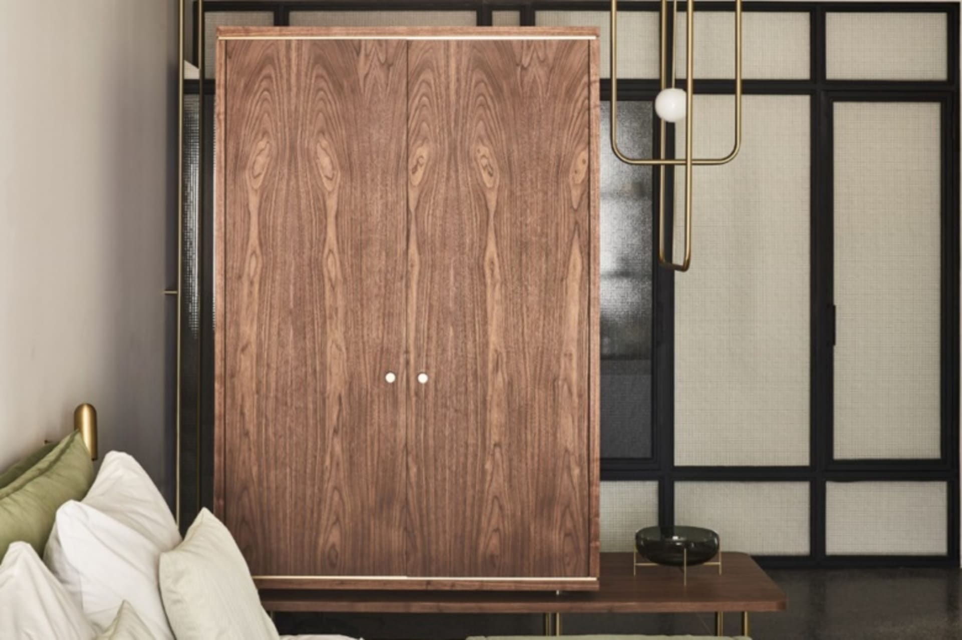 A modern wooden cabinet with two doors and metallic accents, illuminated by pendant lights.