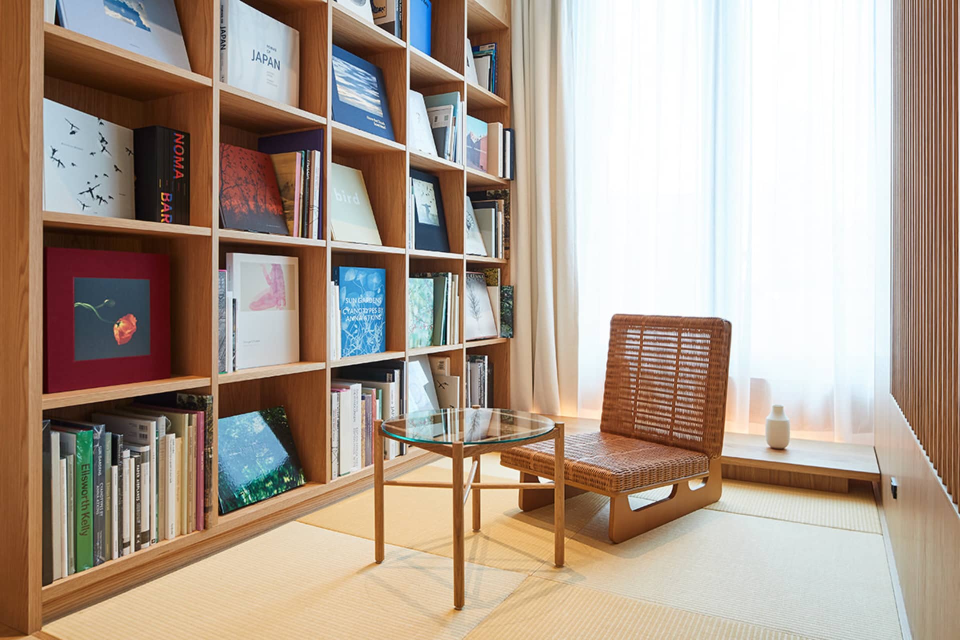 A modern room with a wooden bookshelf, rattan chair, and glass table.
