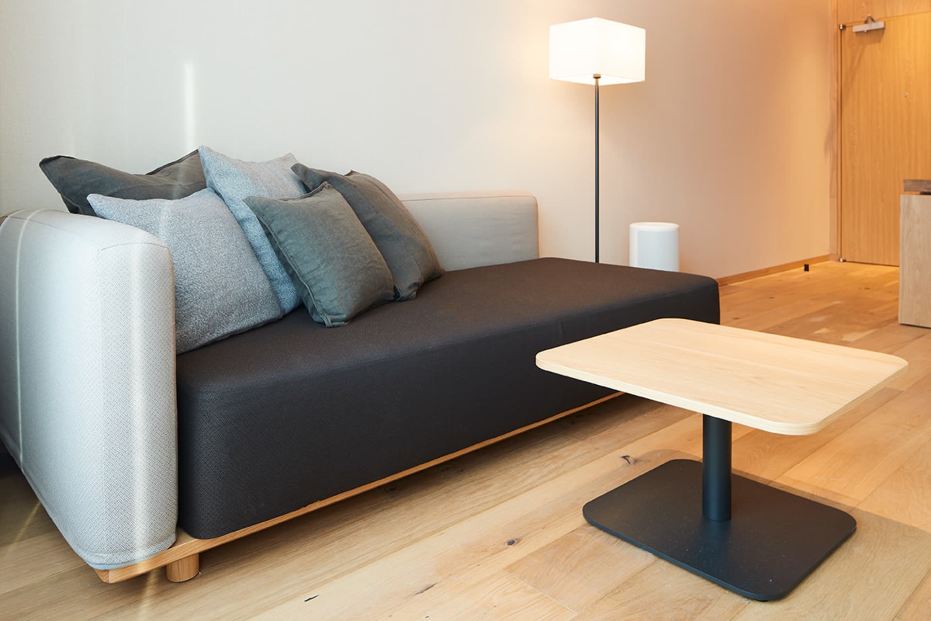 A modern living room with a dark grey couch and wooden coffee table, featuring exposed concrete and wood materials.