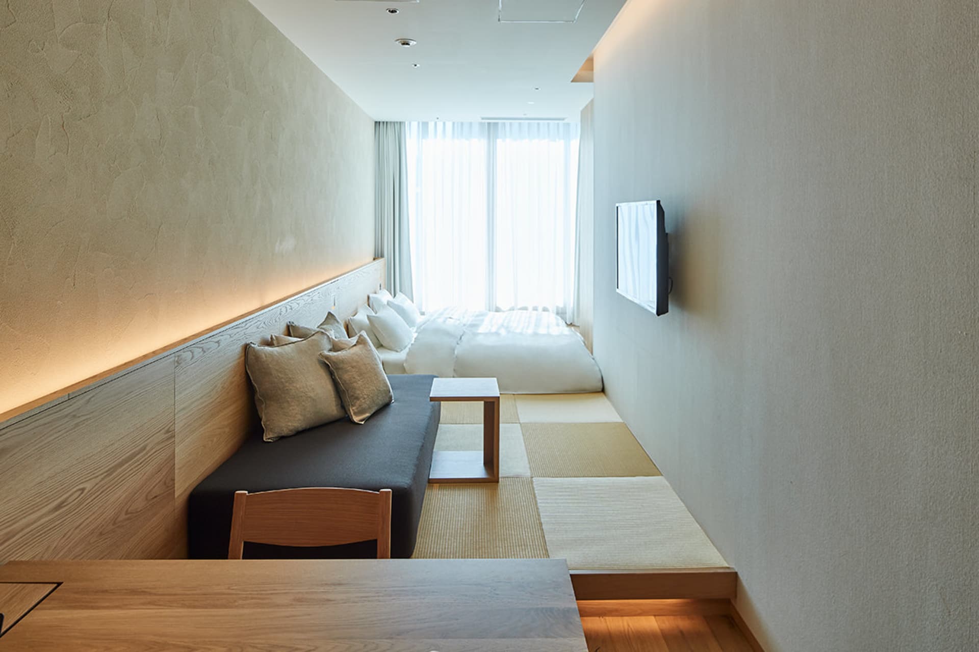 Modern minimalist bedroom with a white bed, wooden table, and minimalist design.