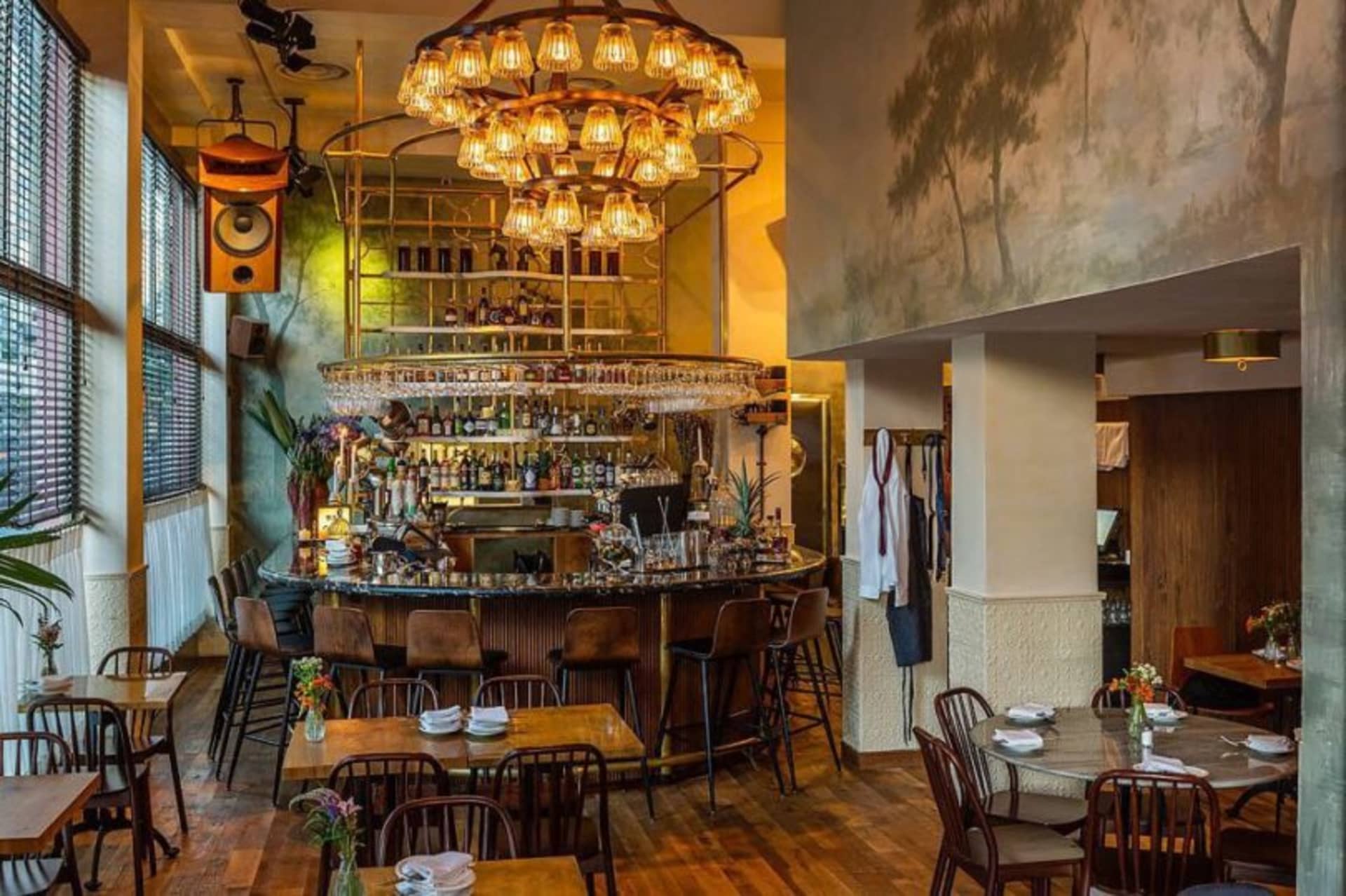 A modern restaurant with wooden tables, metal chairs, and a glass chandelier.