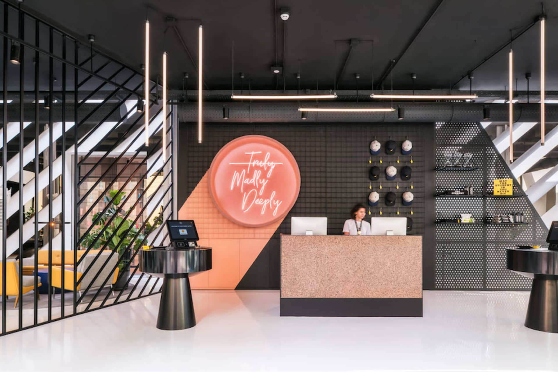 A modern lobby featuring concrete walls and floors, with a reception desk and neon sign