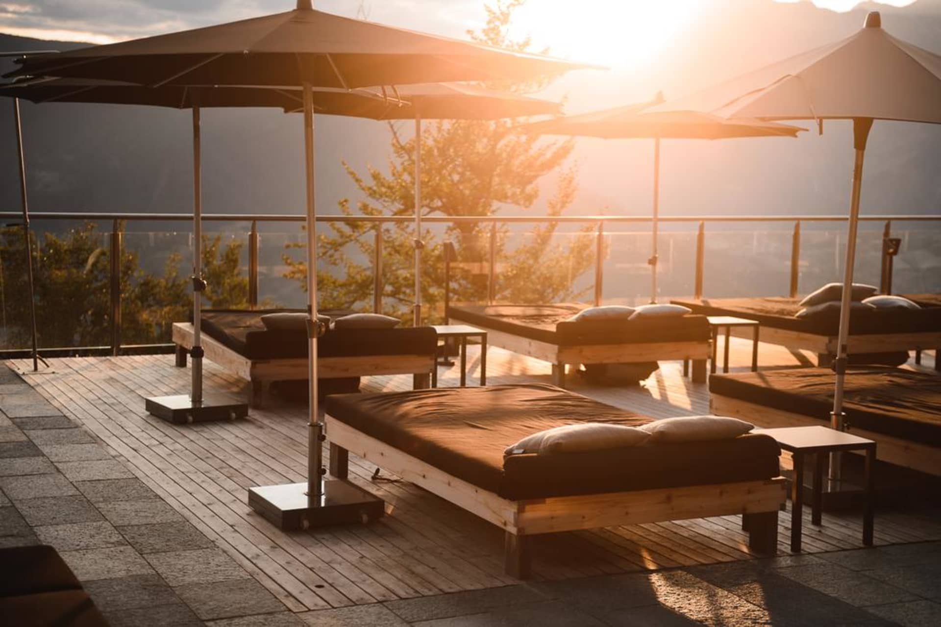 Modern, minimalist outdoor relaxation area with wooden beds, large umbrellas, and a scenic view during sunset.