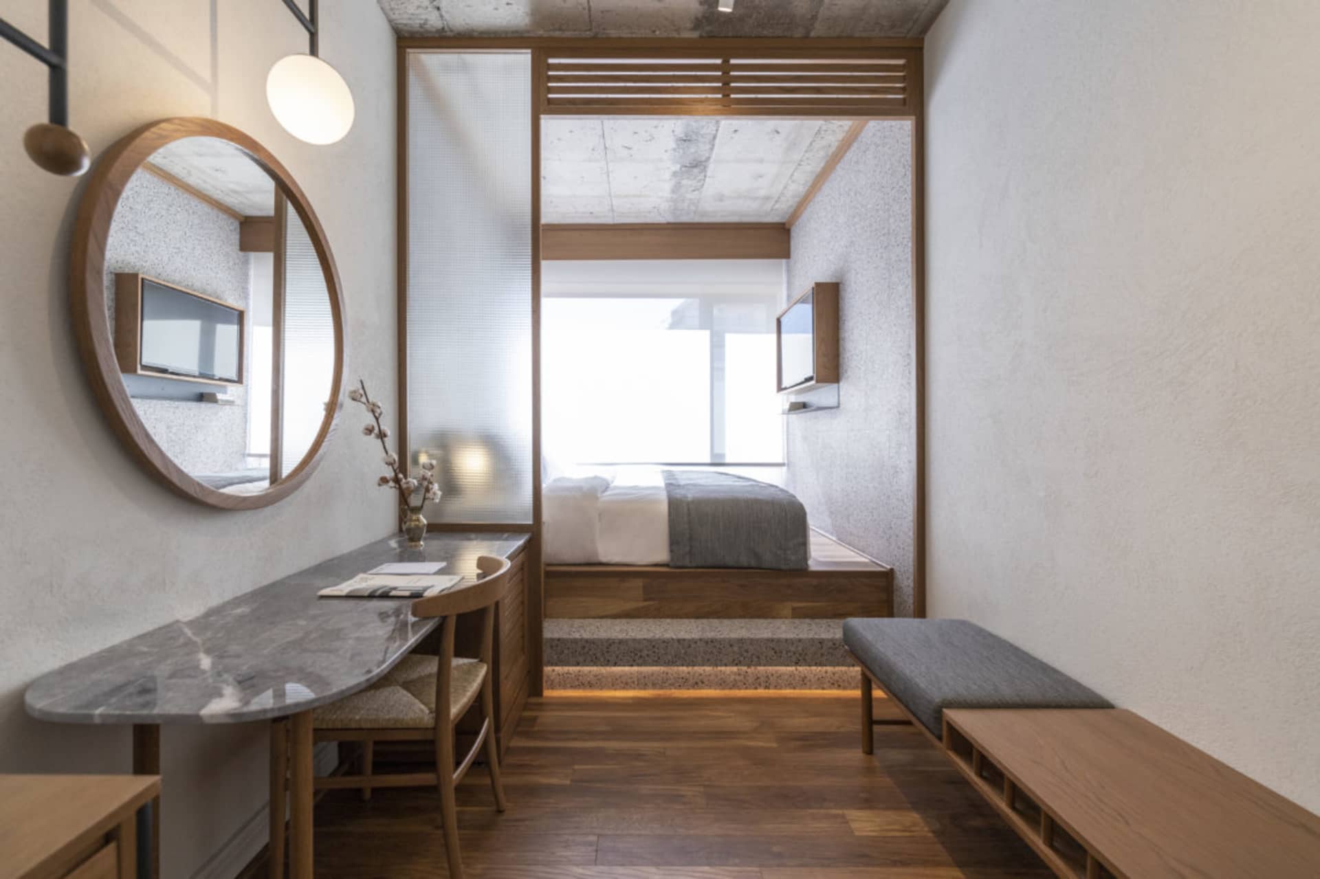 A minimalist bedroom featuring a concrete floor, wooden furniture, and a marble table with a vase of flowers.