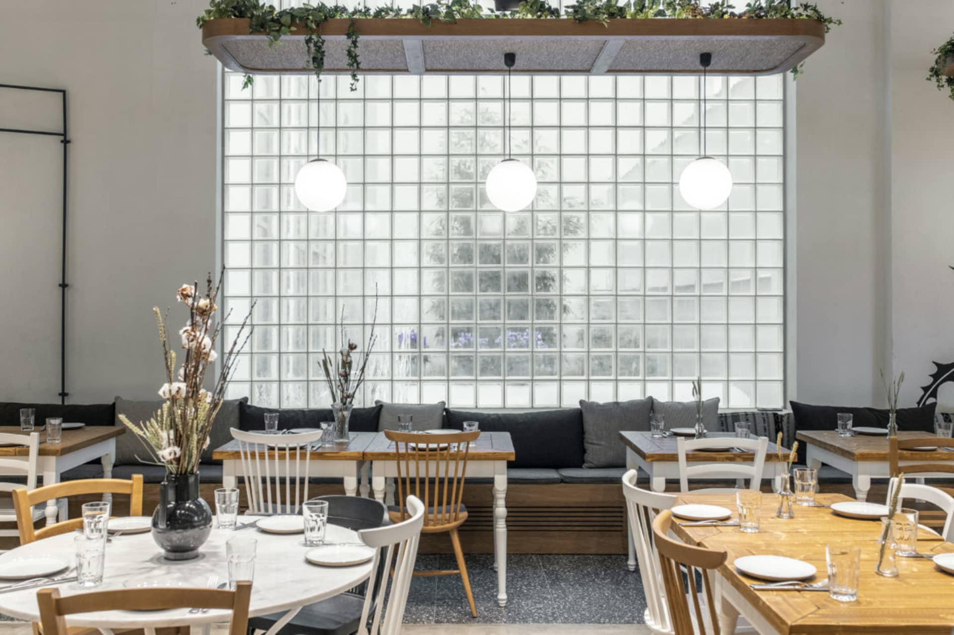 A modern cafe interior with white walls, glass block wall, wood and white tables, and bench seating.