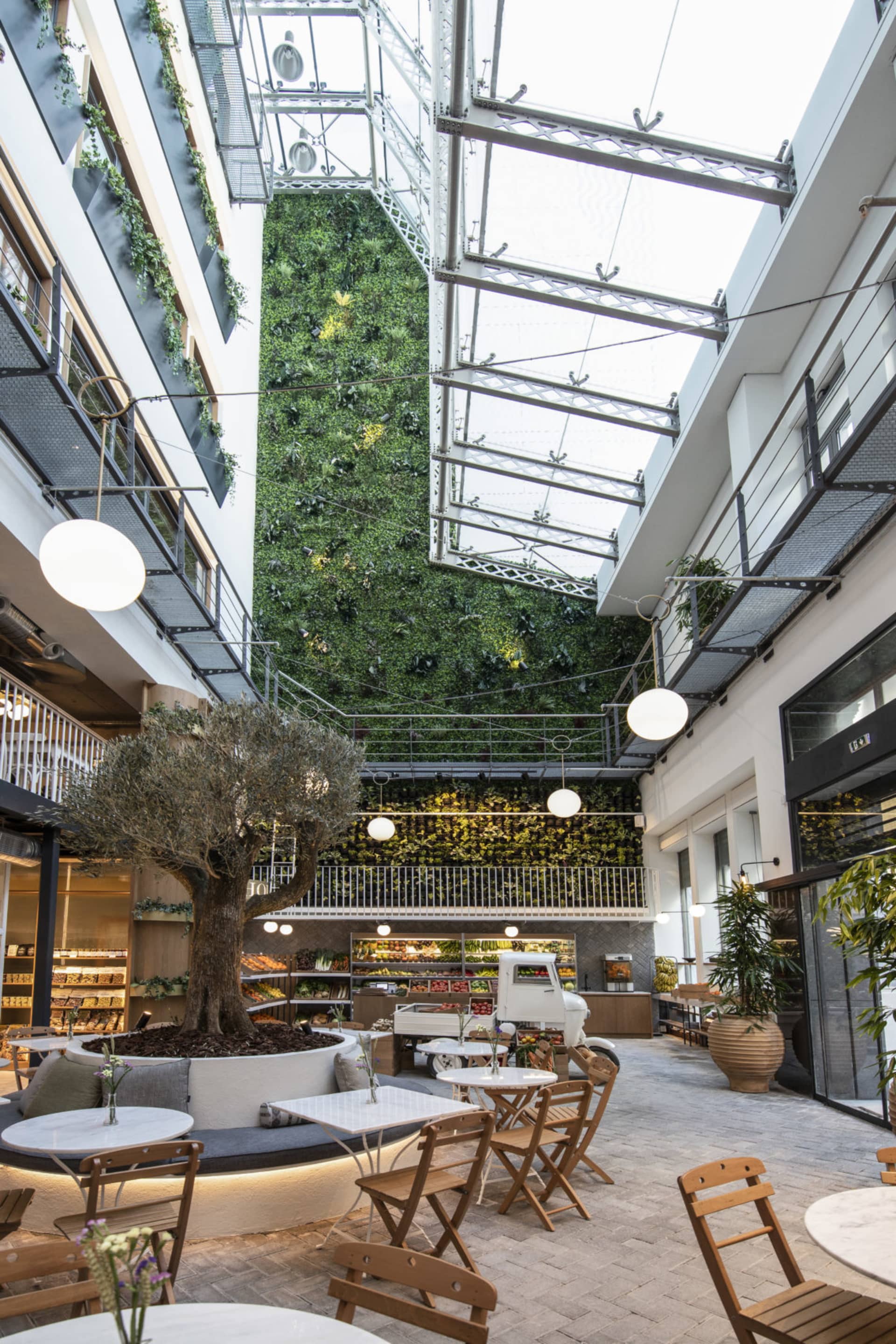 A modern cafe restaurant with concrete floors, walls, and ceiling, featuring a vertical garden wall, wooden furniture, and po