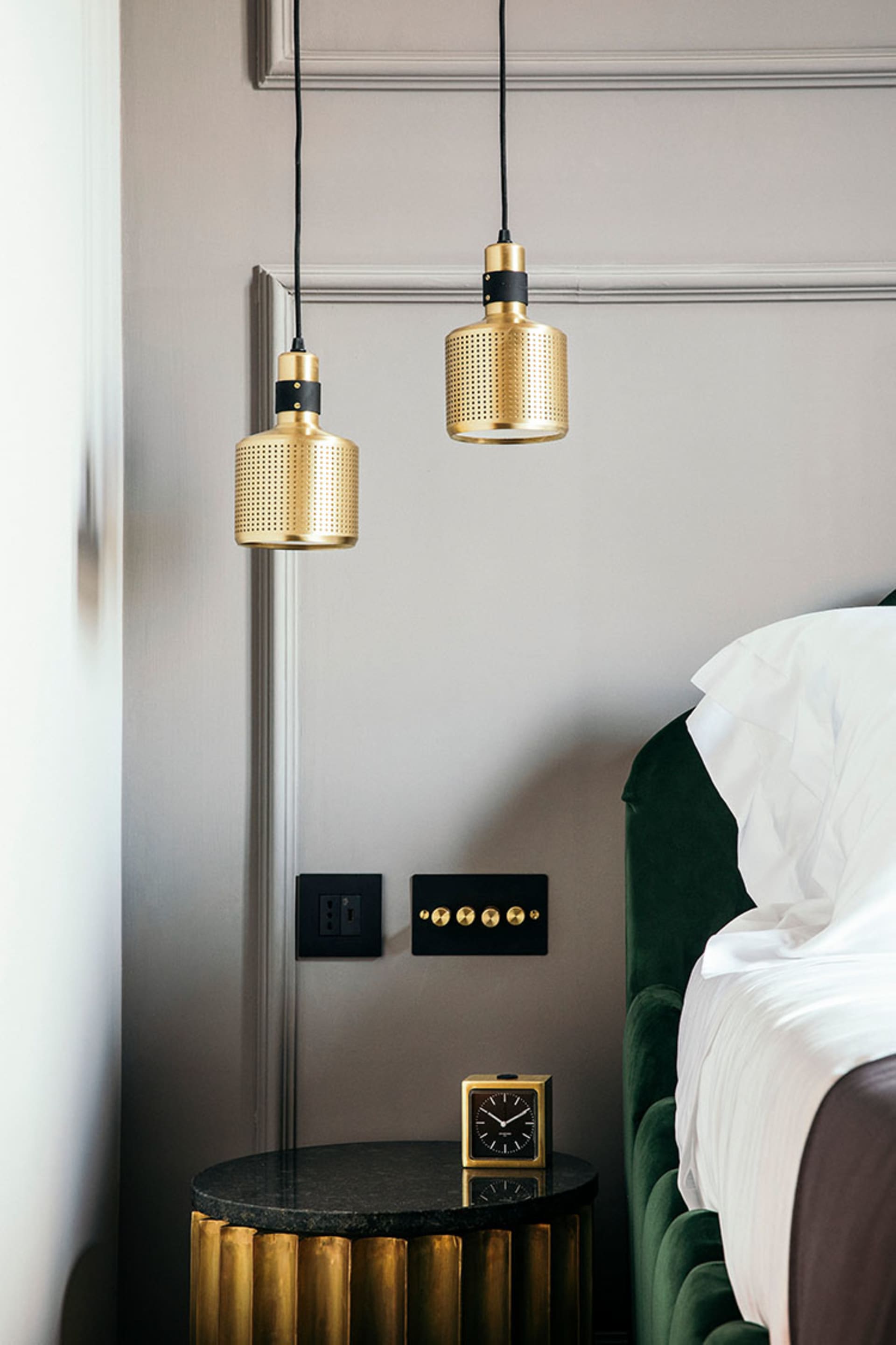 A modern bedroom featuring metallic pendant lights and a leather upholstered headboard against a grey wall with a black side 