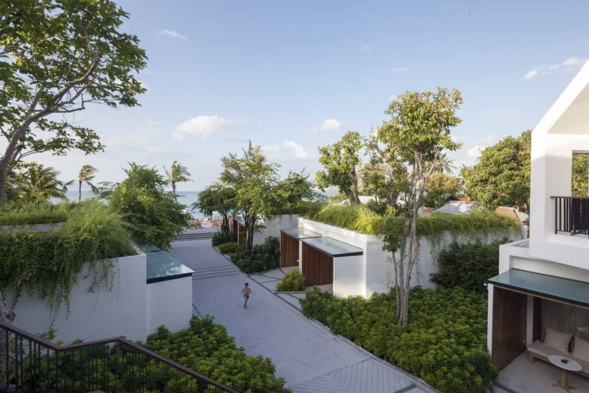 An aerial view of a modern residential house with a green roof and surrounding landscaping, under a clear blue sky.