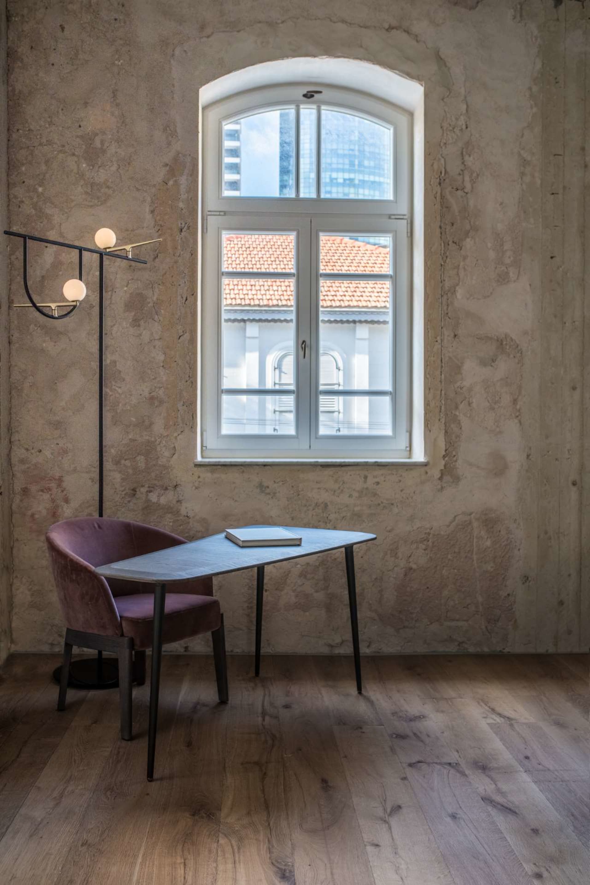 A modern workspace with a concrete table and pink chair, featuring a book on the table and a floor lamp.