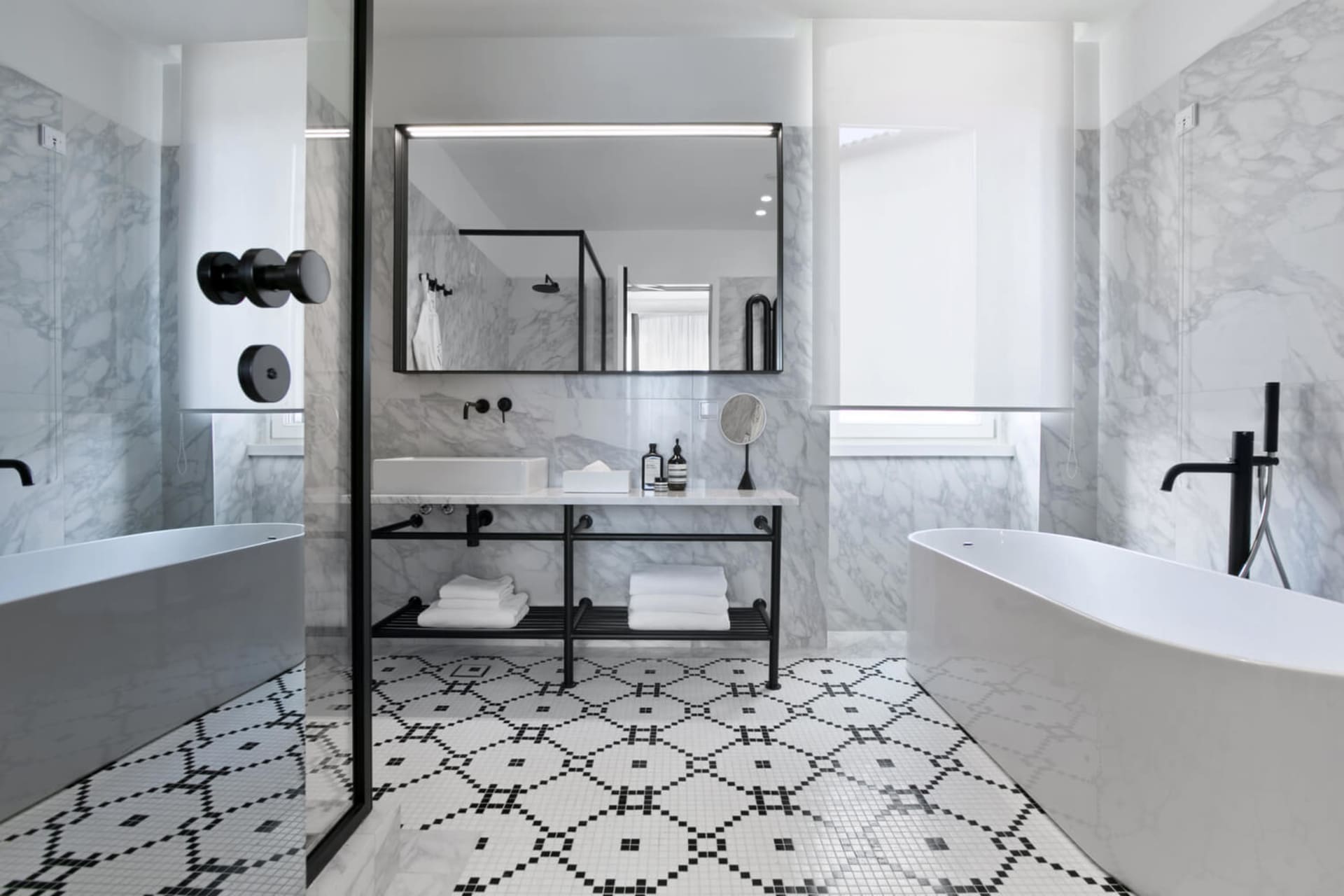 A modern bathroom with marble walls, mosaic floor tiles, and a freestanding bathtub.