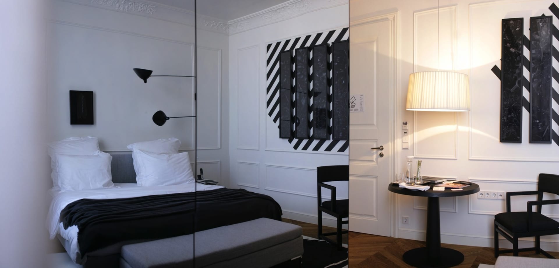 A modern bedroom featuring black and white decor, with a bed, bench, and lamp.