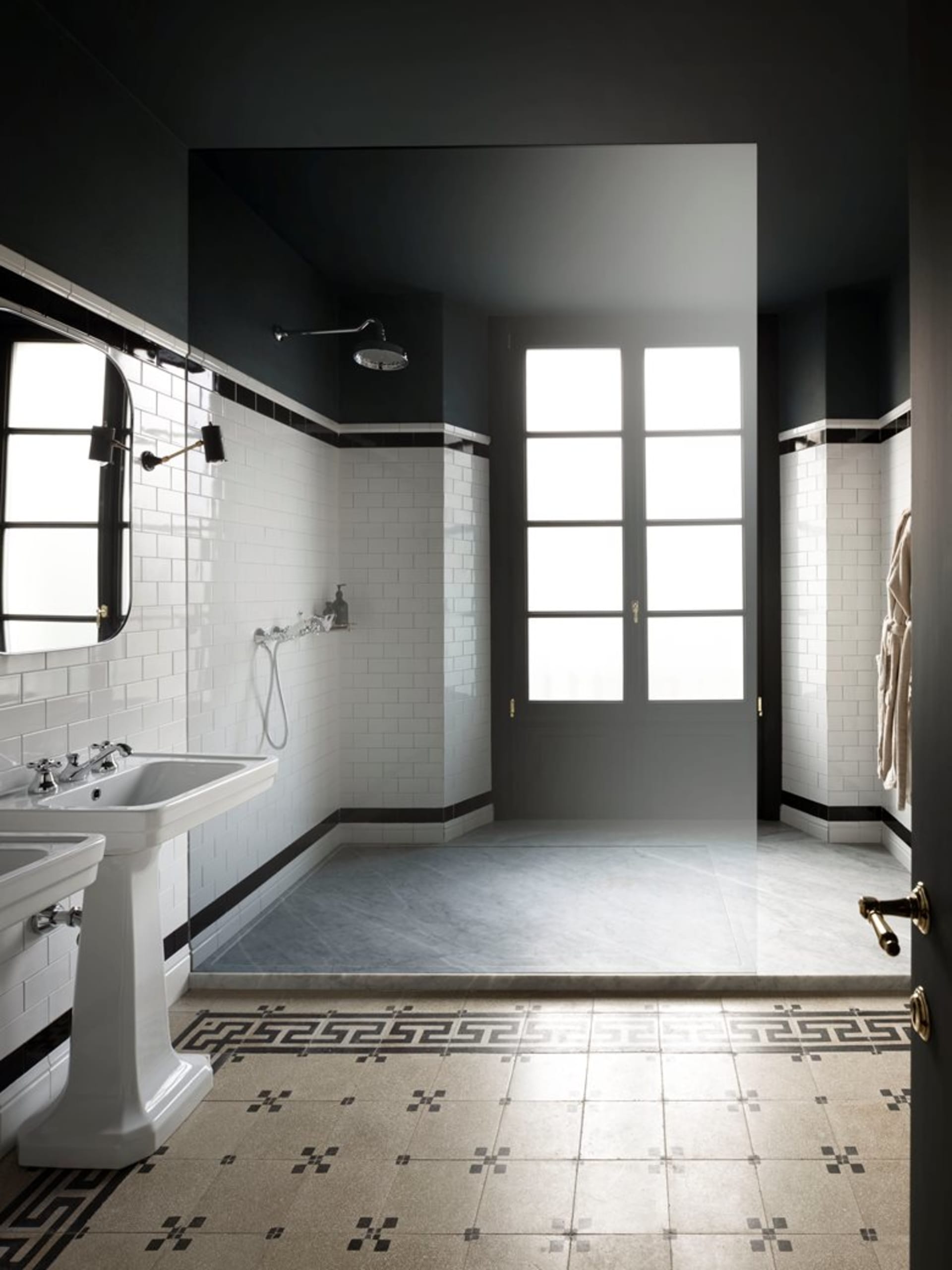 An industrial-style bathroom with white tiles, featuring a shower area, a pedestal sink, and a glass door.