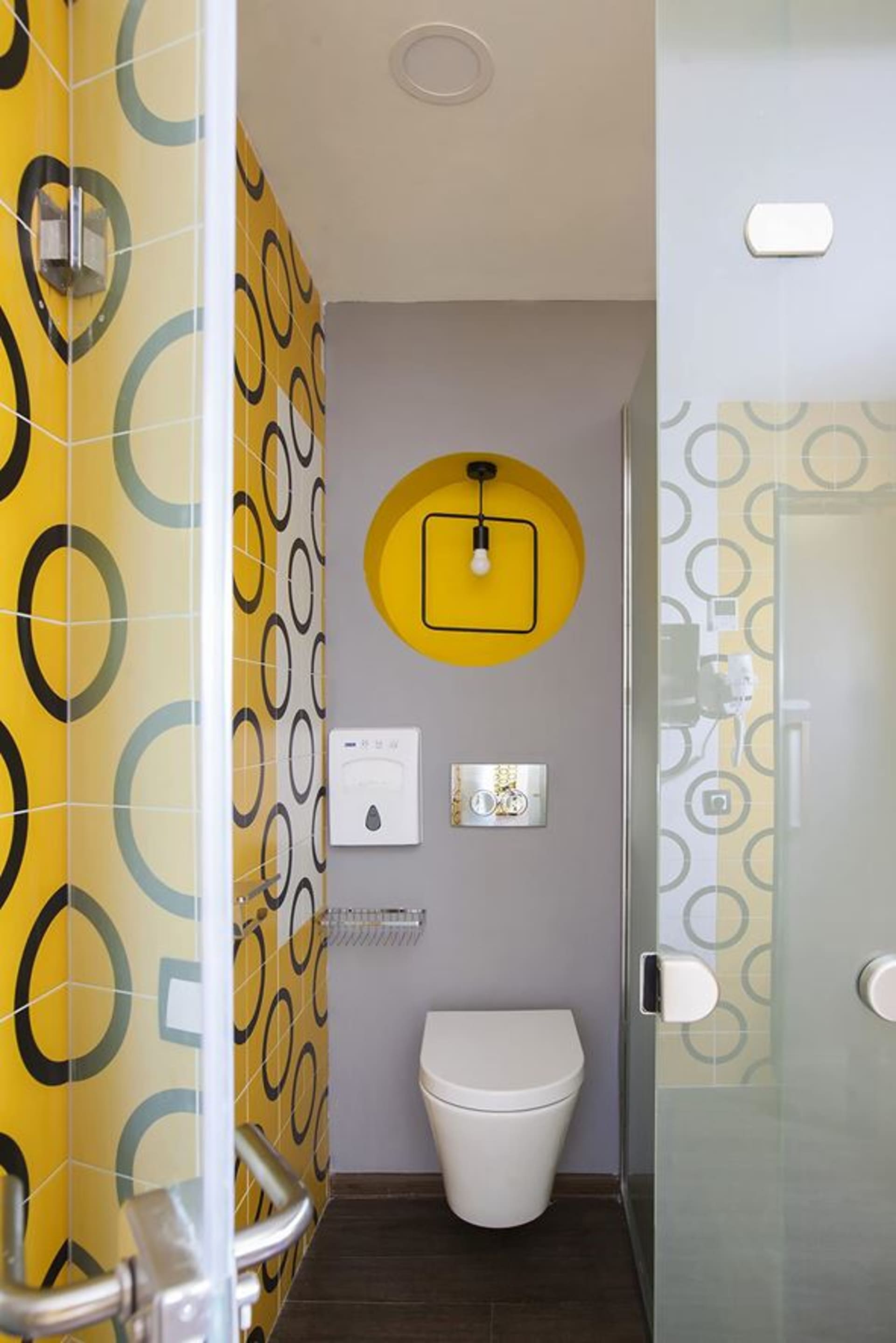 A contemporary bathroom with yellow patterned tiles, a white toilet, and a circular light fixture.
