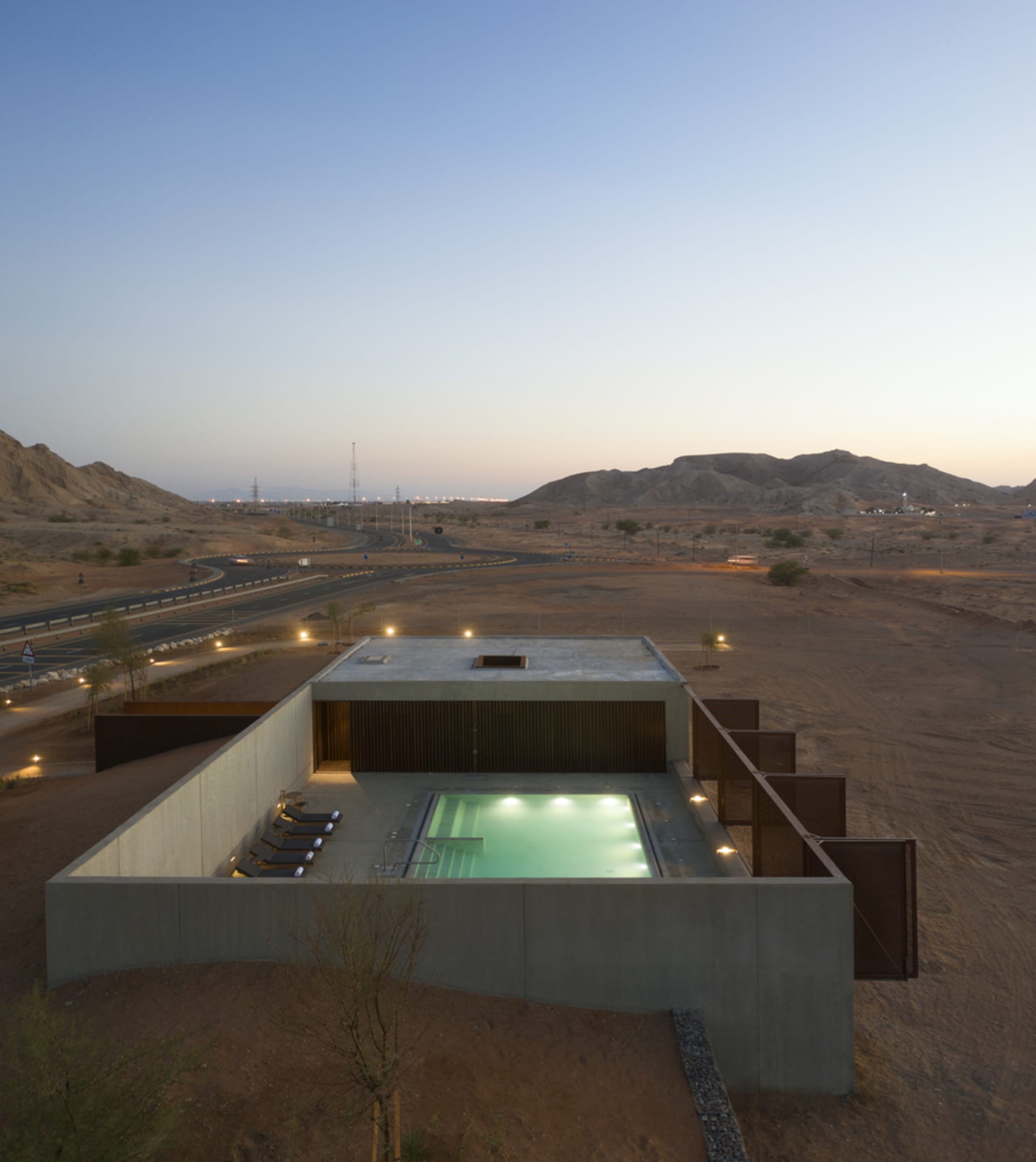 Modern concrete structure with a pool and lounge area in a desert landscape.