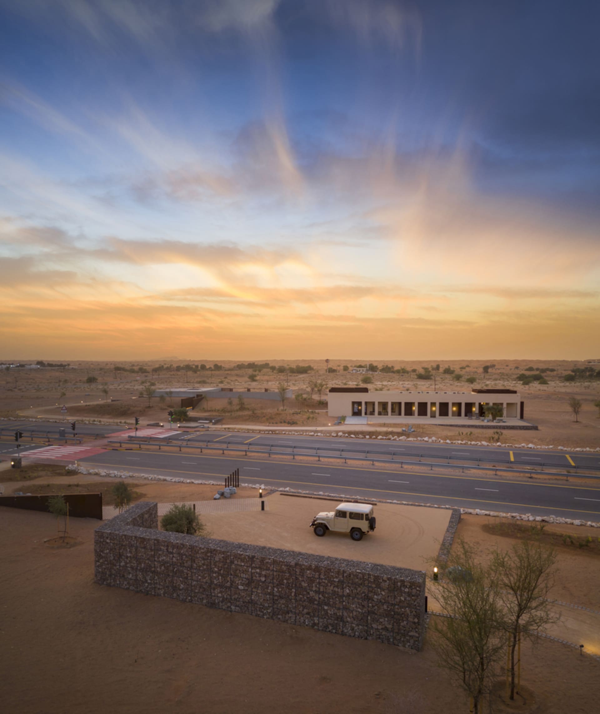 A desert landscape with a roadway and a building at sunset.