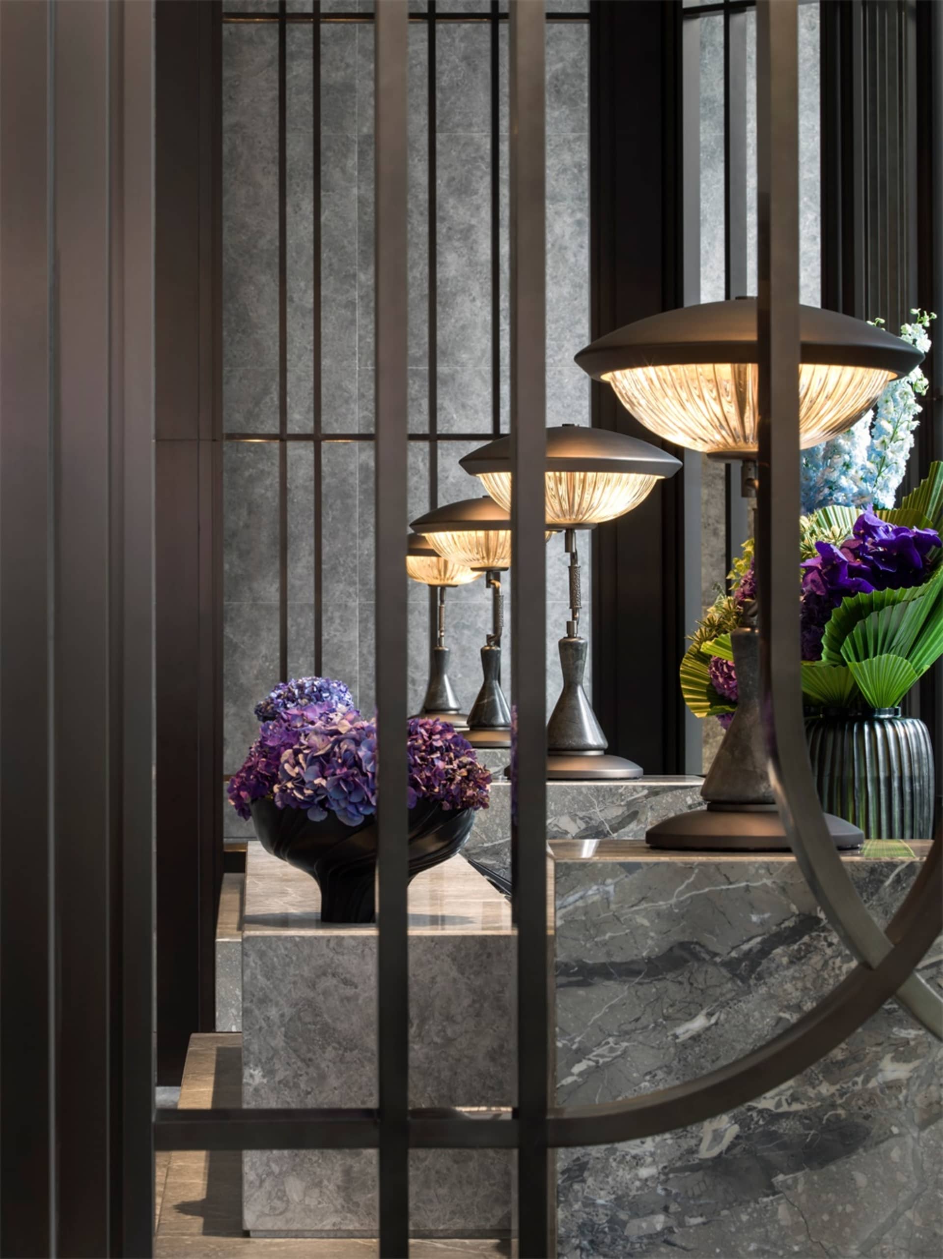 A modern hotel lobby featuring marble surfaces and metal accents with a bouquet of purple flowers on display.