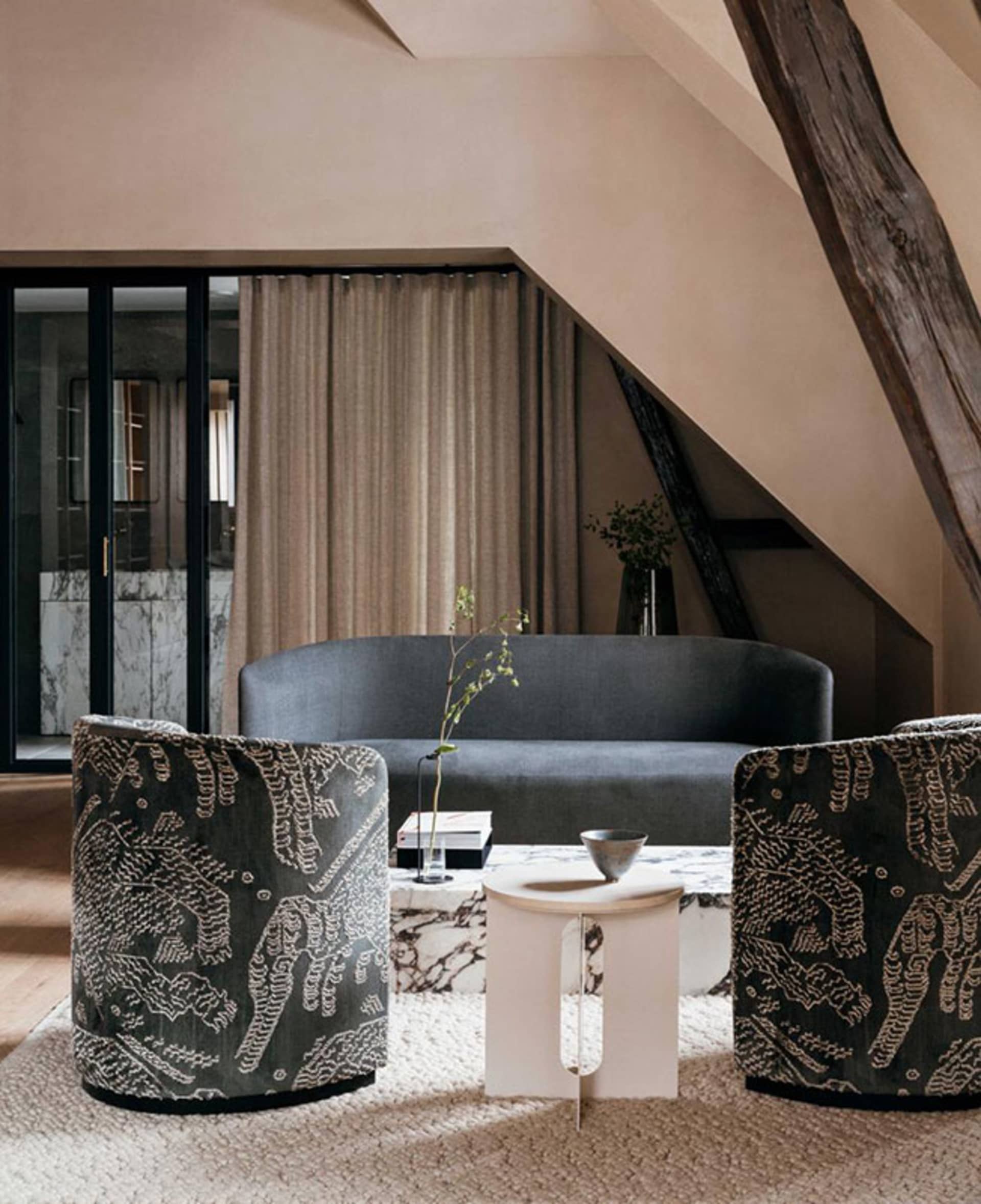 A modern living room with grey upholstered furniture, patterned chairs, and a marble coffee table.