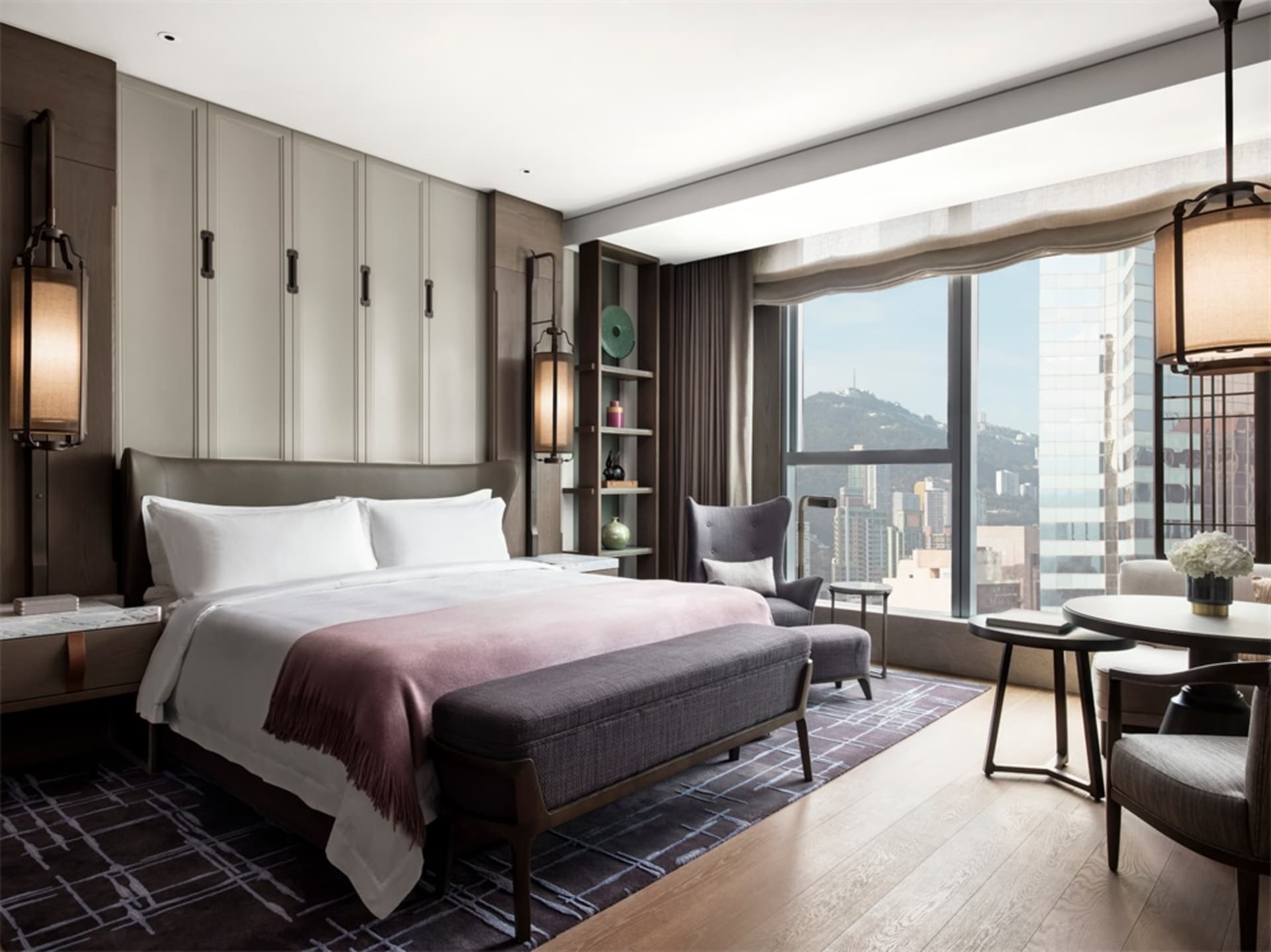 Modern, luxurious bedroom featuring a king-sized bed with a city view through large windows.