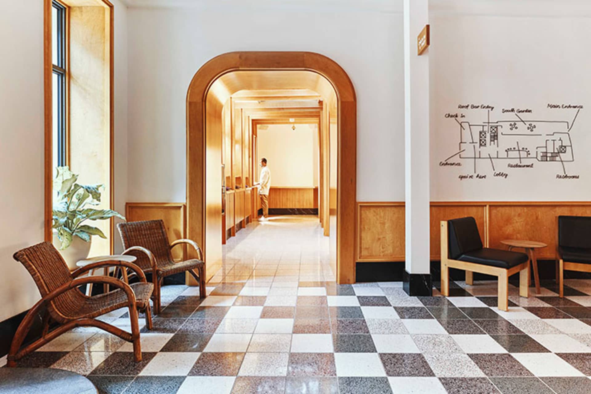 A spacious, terrazzo-floored and wood-paneled hospitality interior with a seating area and a hallway leading deeper into the