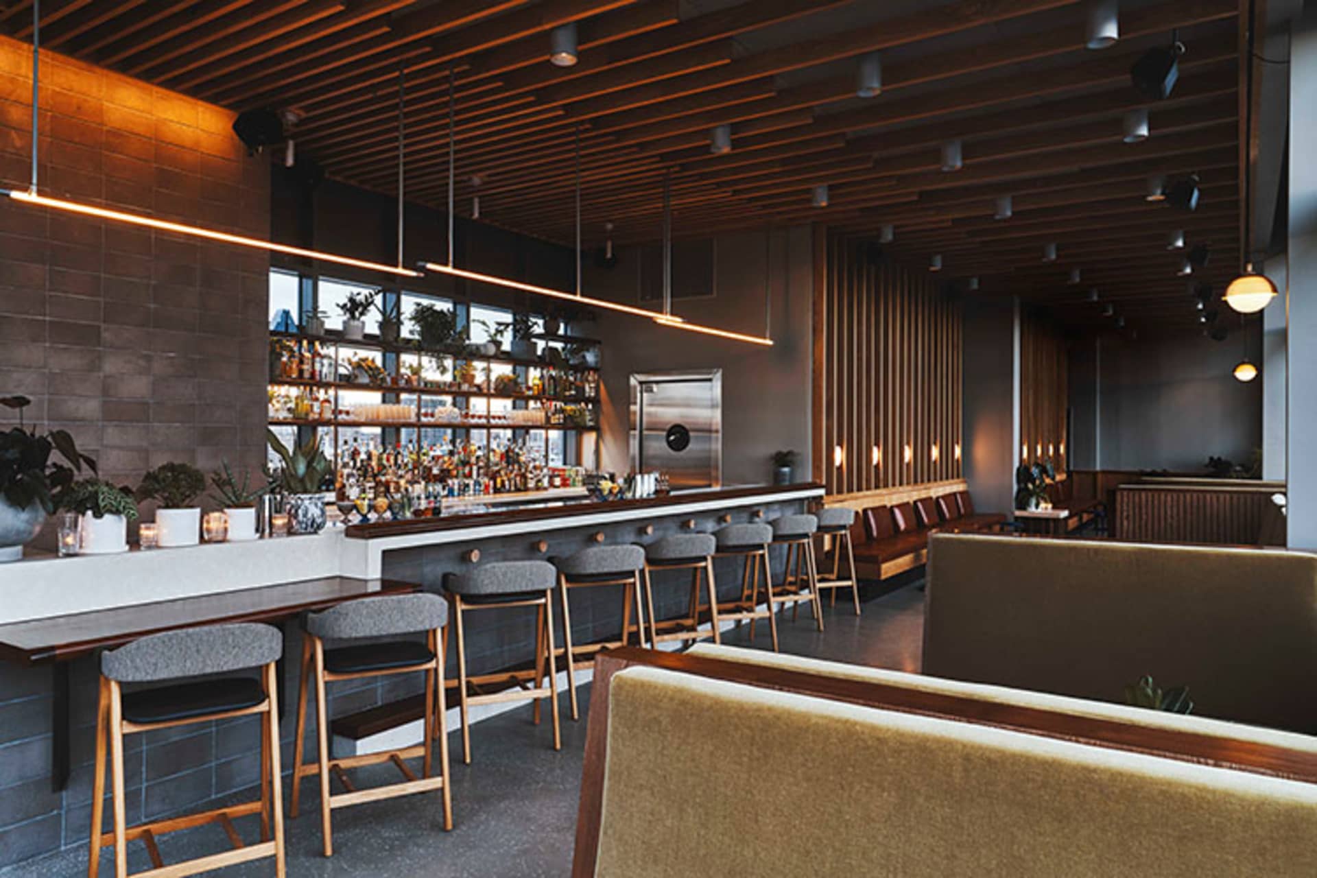 A modern restaurant bar interior featuring wooden walls, leather seating, and concrete flooring.