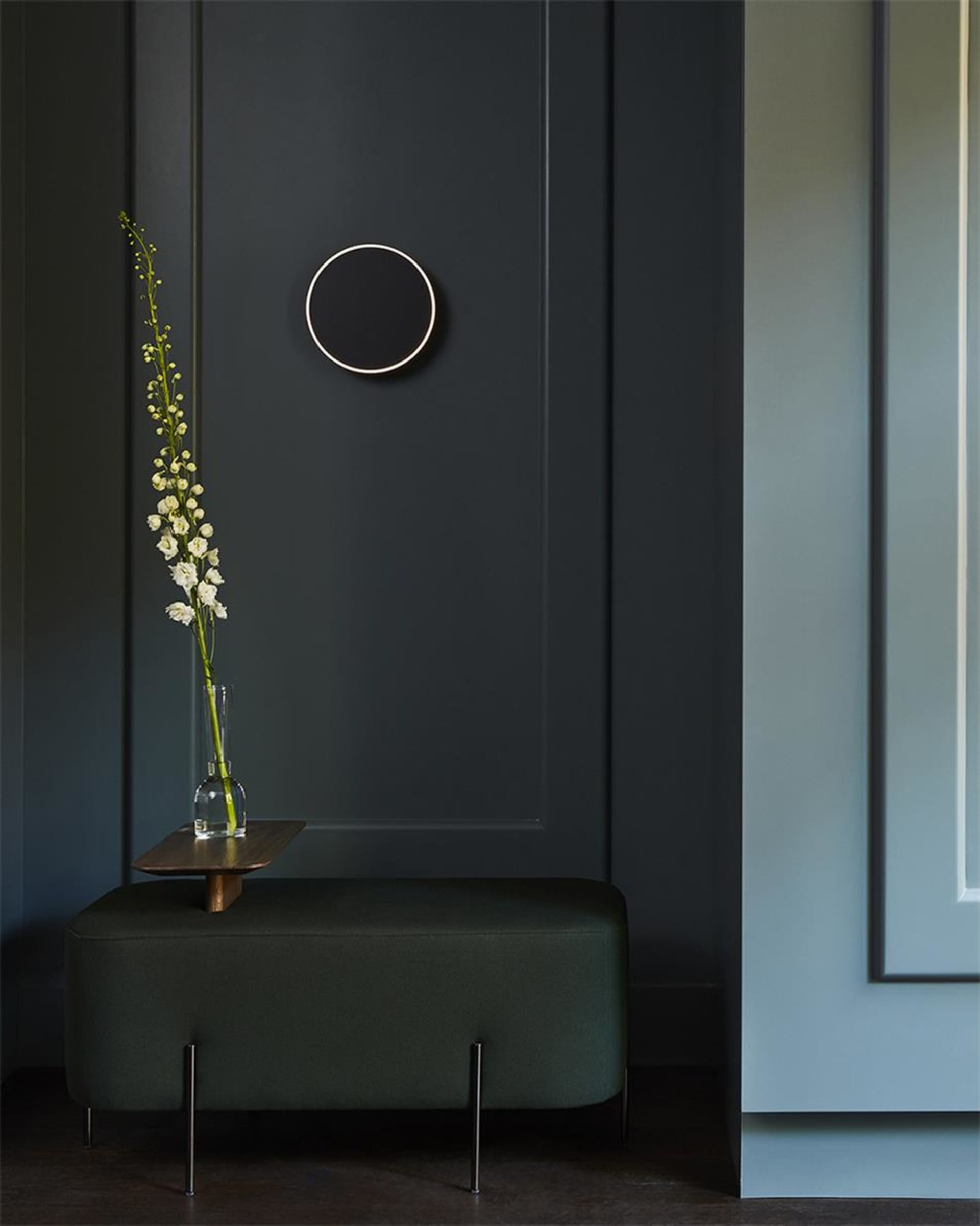 A modern entryway with a dark wooden bench and a vase of flowers placed on a small wooden table in front of a dark-paneled wa