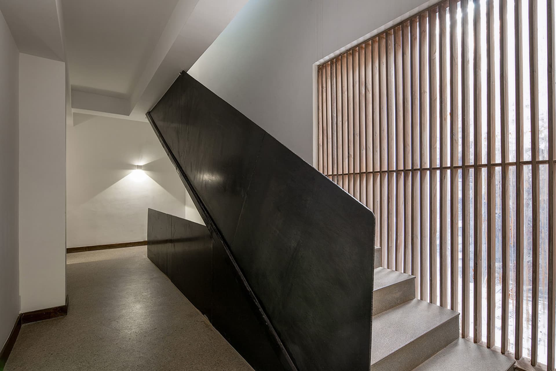 A minimalist black steel staircase with a wooden slatted wall in the background.