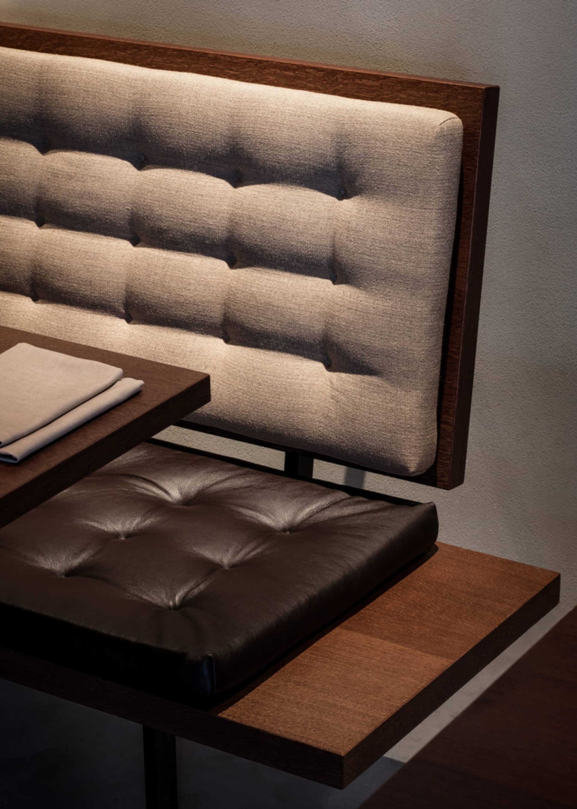 A modern bench seat with a tufted fabric backrest and a brown leather cushion on a wooden platform.