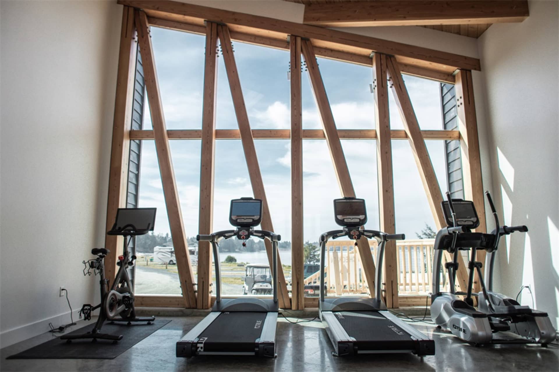 Industrial-style gym with metal treadmills and stationary bikes in front of large windows.