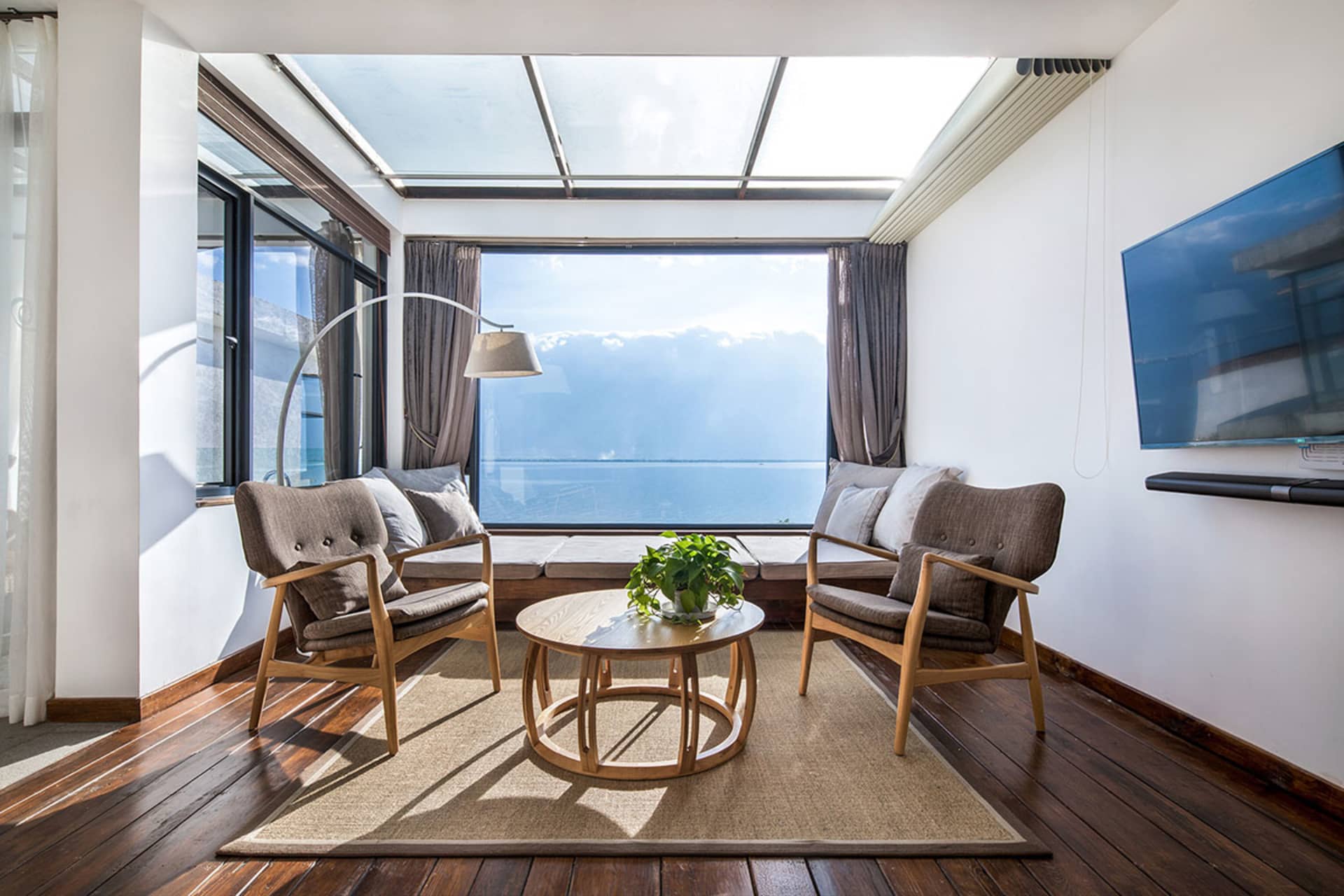 Modern living room featuring a comfortable sofa, table, and potted plant with a scenic marine view through large windows and