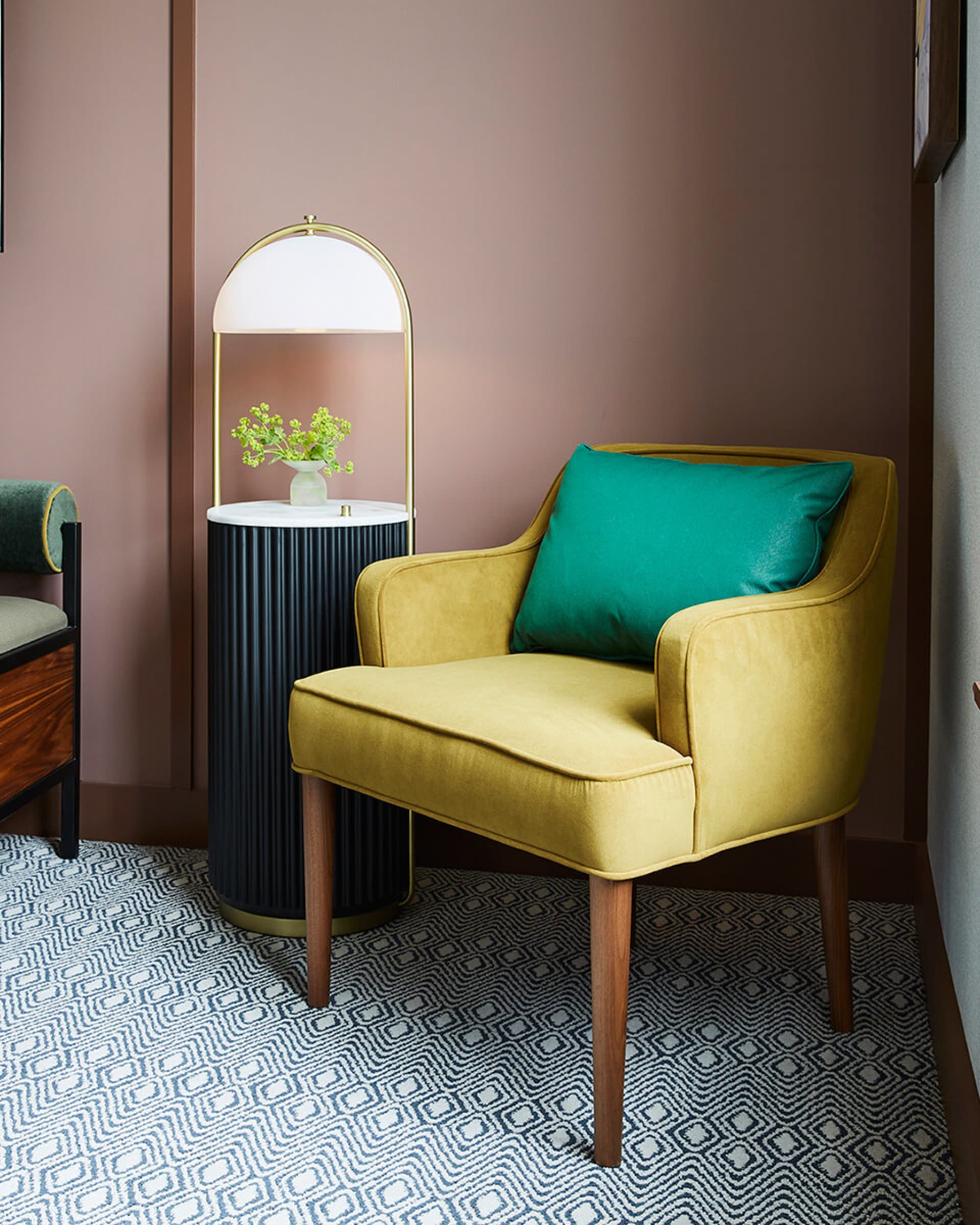 Modern living room with a yellow upholstered armchair featuring a green throw pillow, a marble side table with a brass lamp,