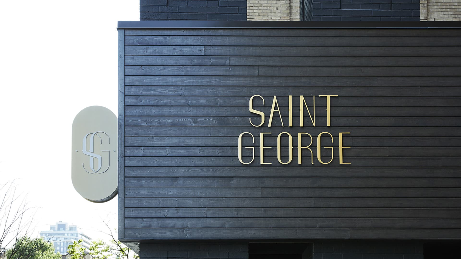 The exterior facade of a modern building with a black wooden exterior and a gold sign reading 'SAINT GEORGE'.