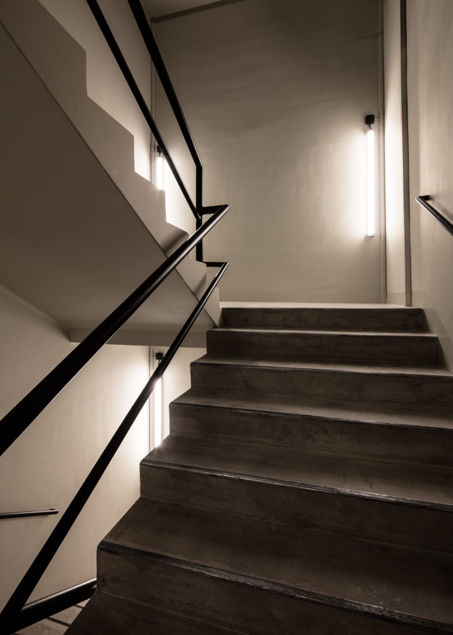 Modern concrete staircase with black metal railing in an interior setting.