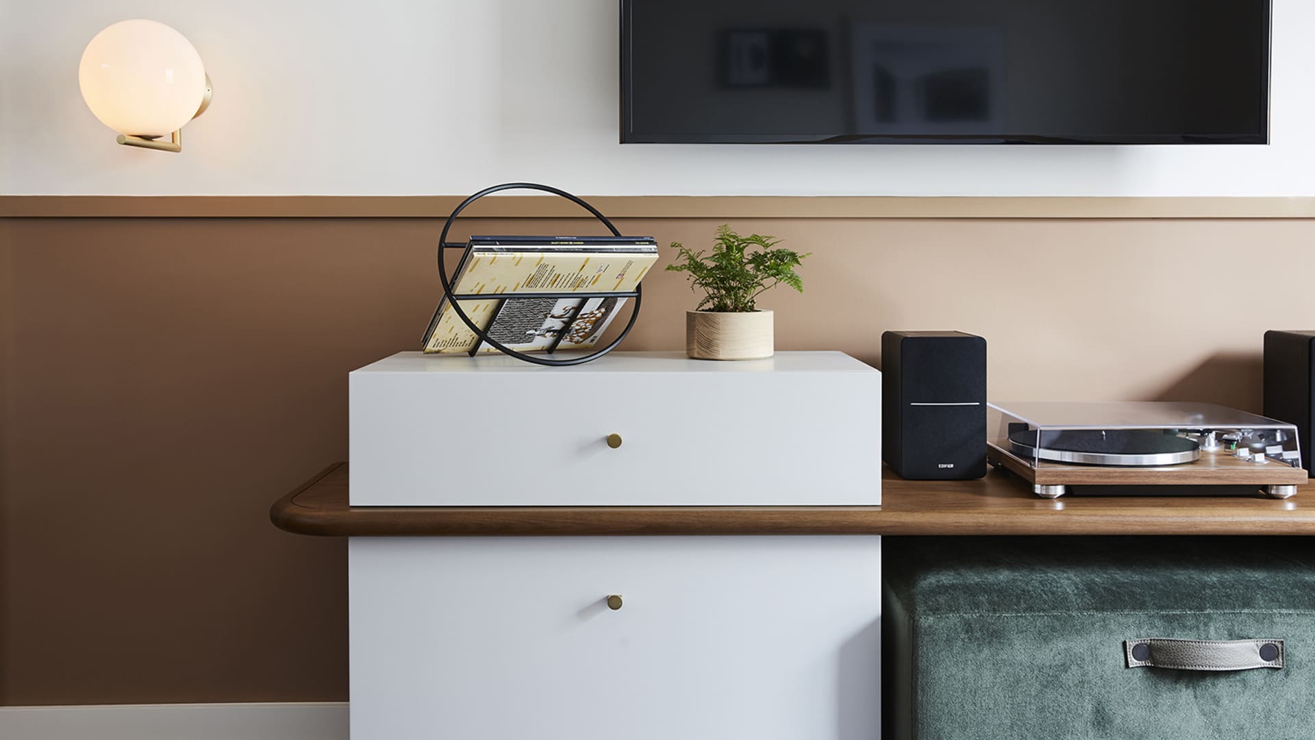 A modern living room featuring a white cabinet, wooden table, green ottoman, and a turntable with speakers.