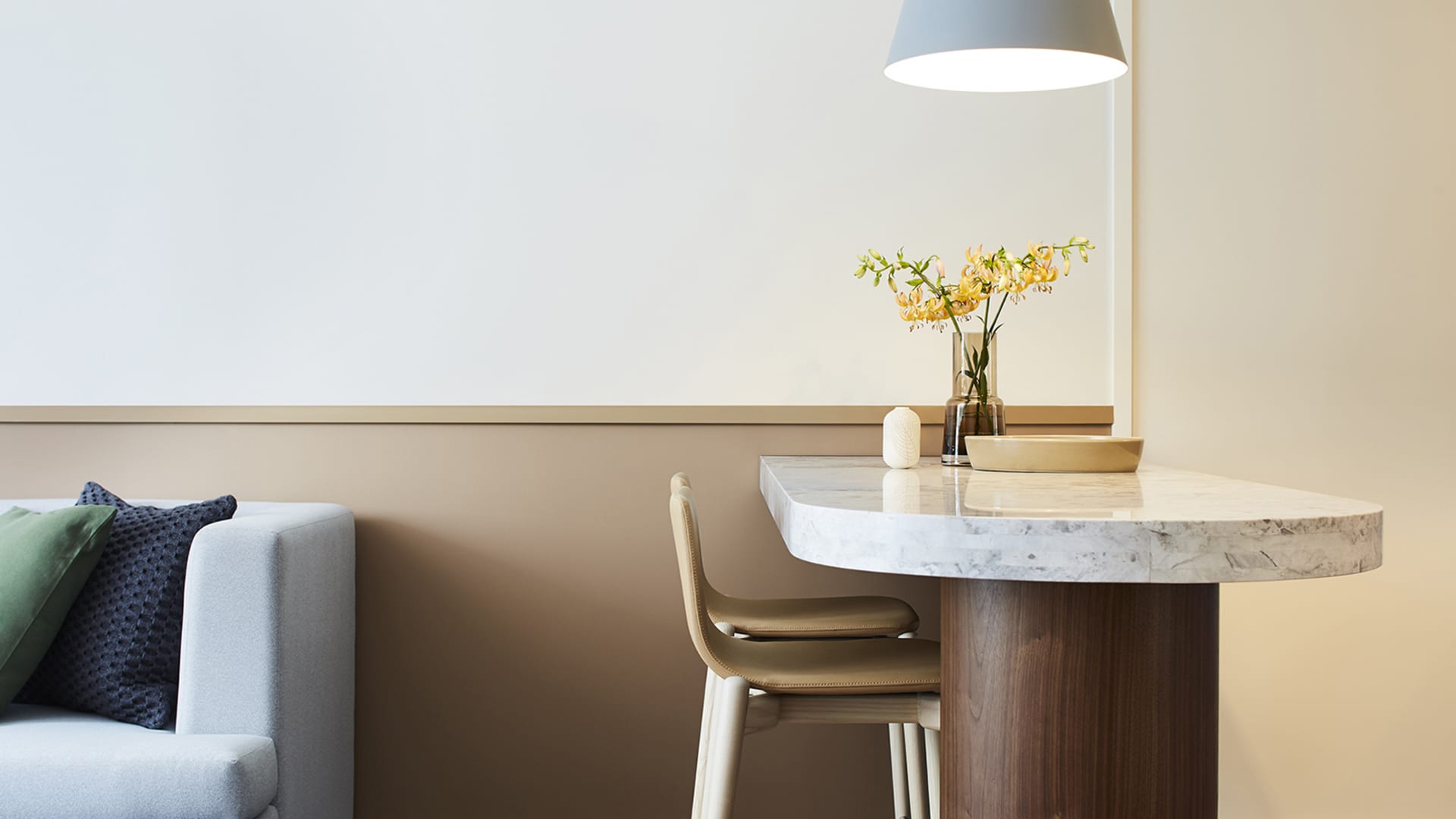 A modern minimalist home office featuring a marble table and wooden chair, with a vase of yellow flowers on the table.