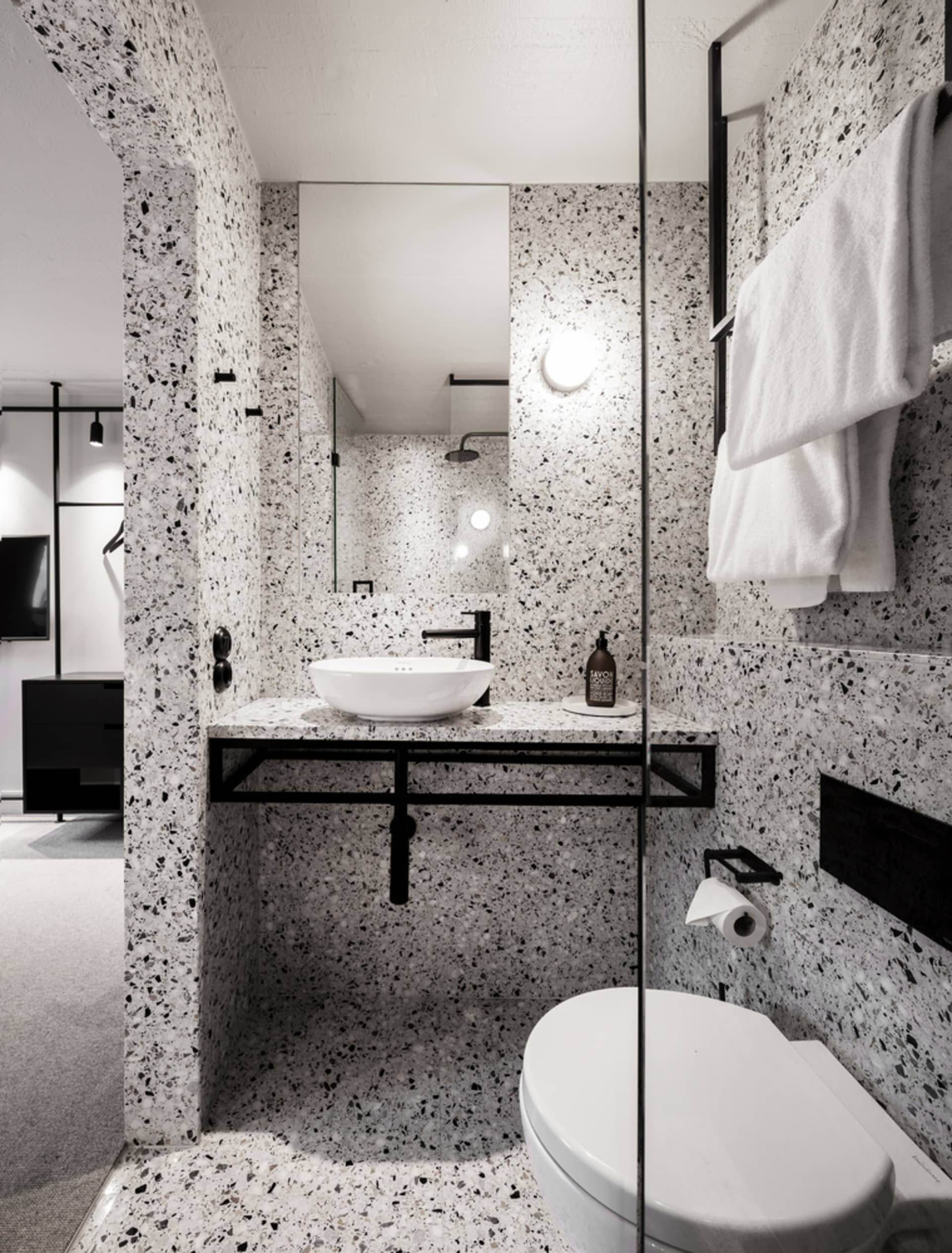 Modern residential bathroom with white and black terrazzo tiles, white sink, and black fixtures.
