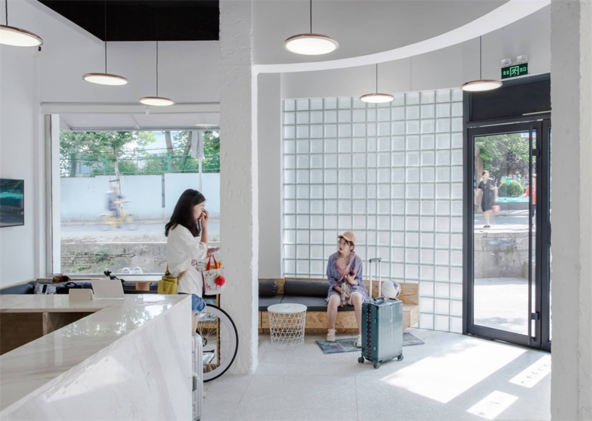 Two women having a conversation in a modern coffee shop with glass brick walls, white countertops, and a bicycle parked near