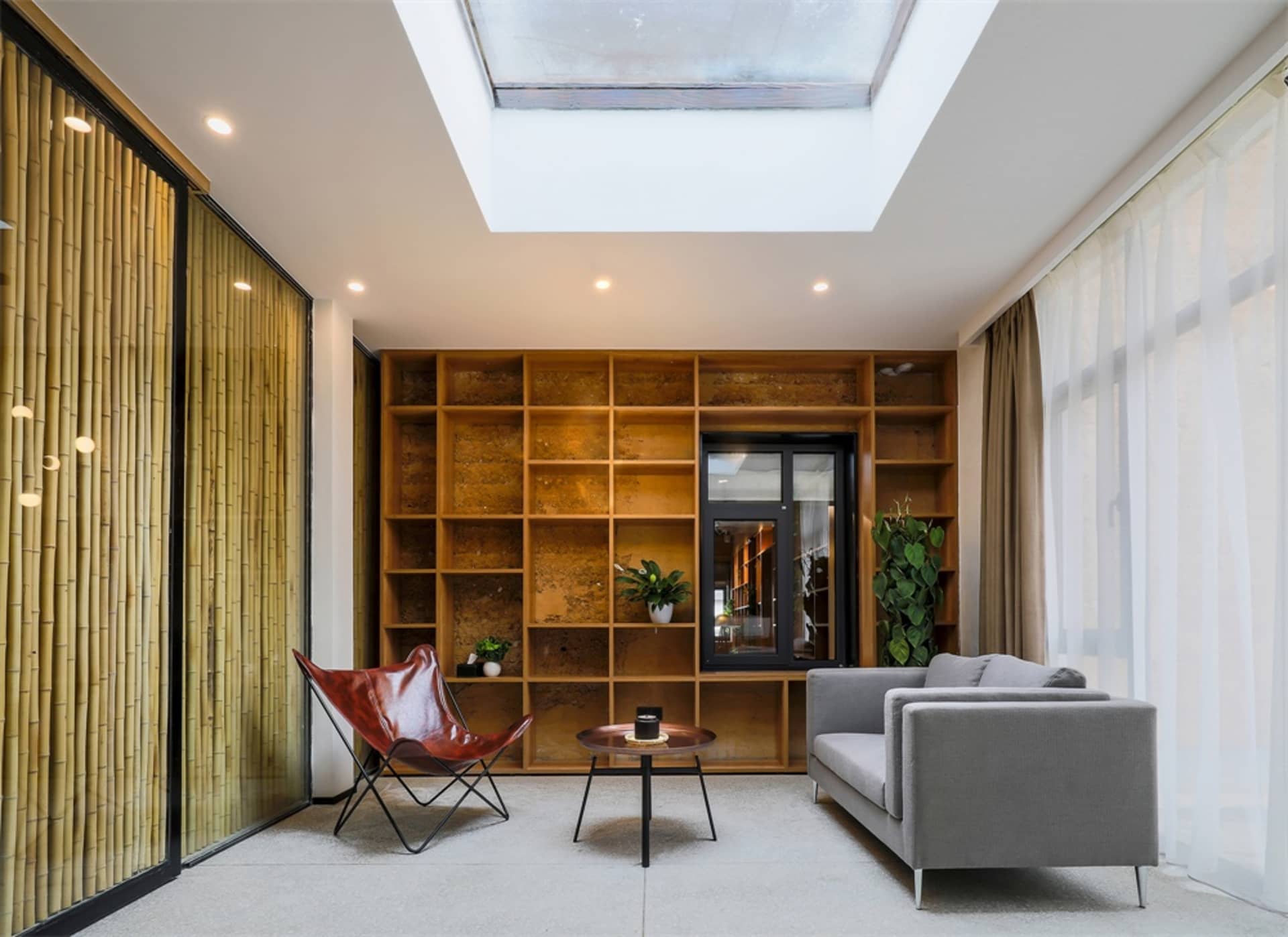 A modern living room featuring wooden shelves, glass windows, and a textile sofa.