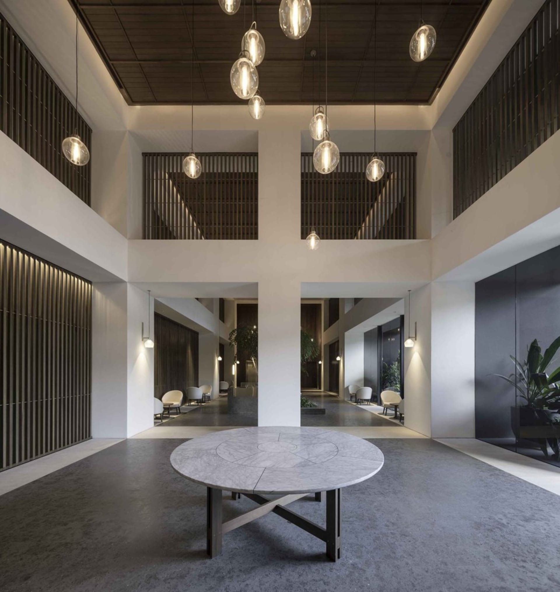 Modern, minimalist lobby interior with a round, white marble table and concrete flooring.