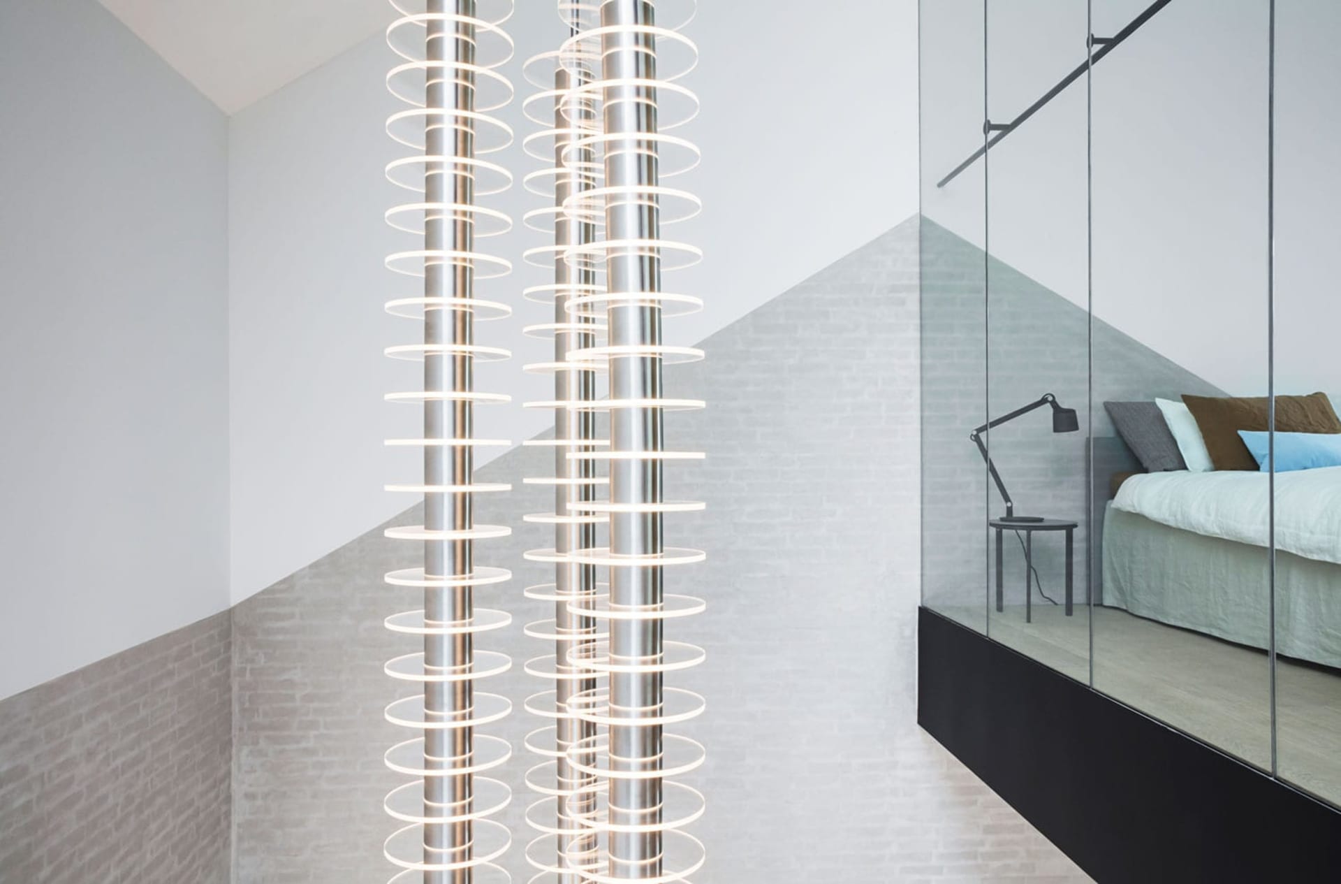 A modern minimalist bedroom with metallic pendant lights and a glass partition.