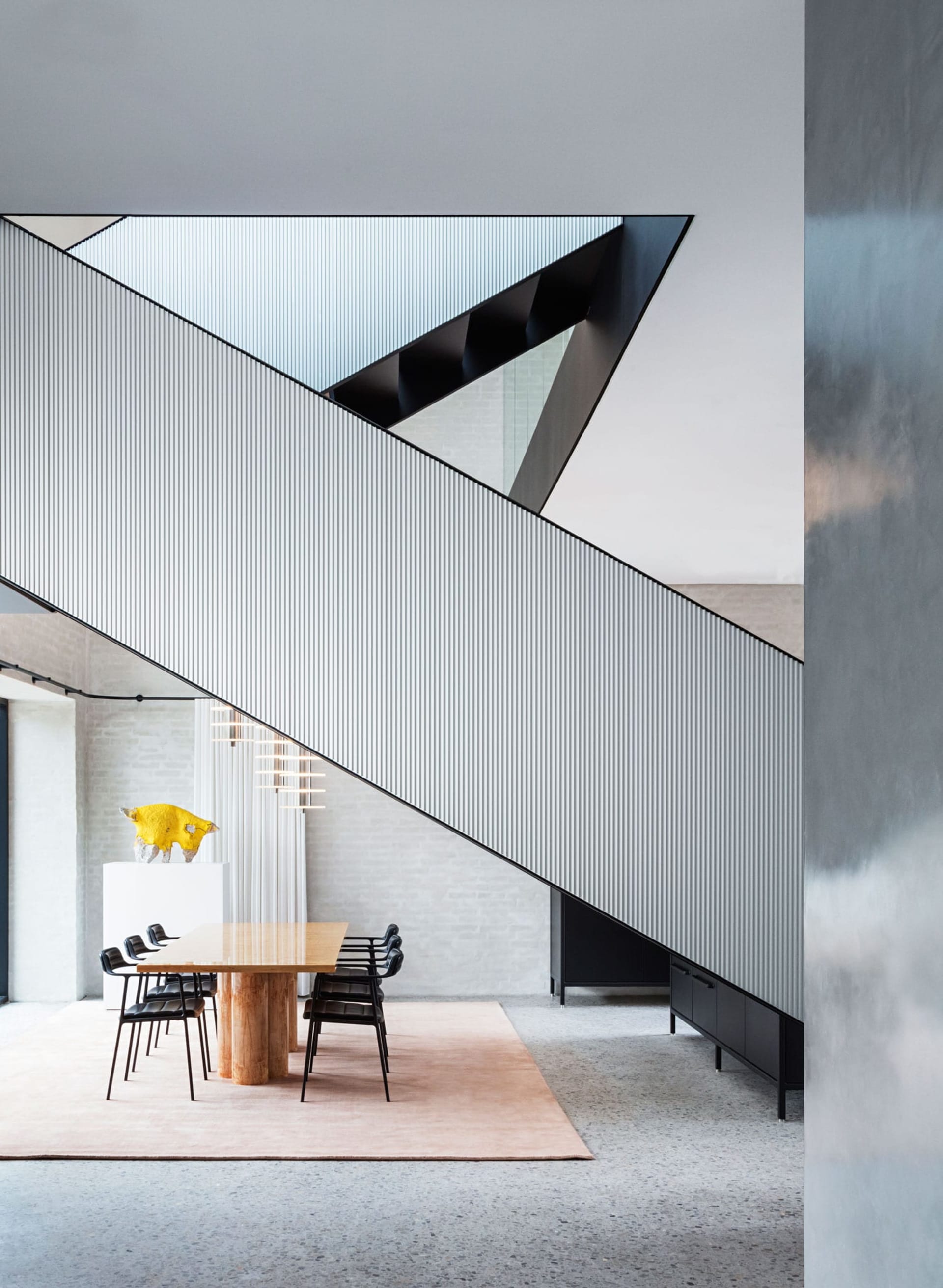 A modern minimalist dining room with a geometric design featuring a contemporary wooden dining table, black chairs, and a tex