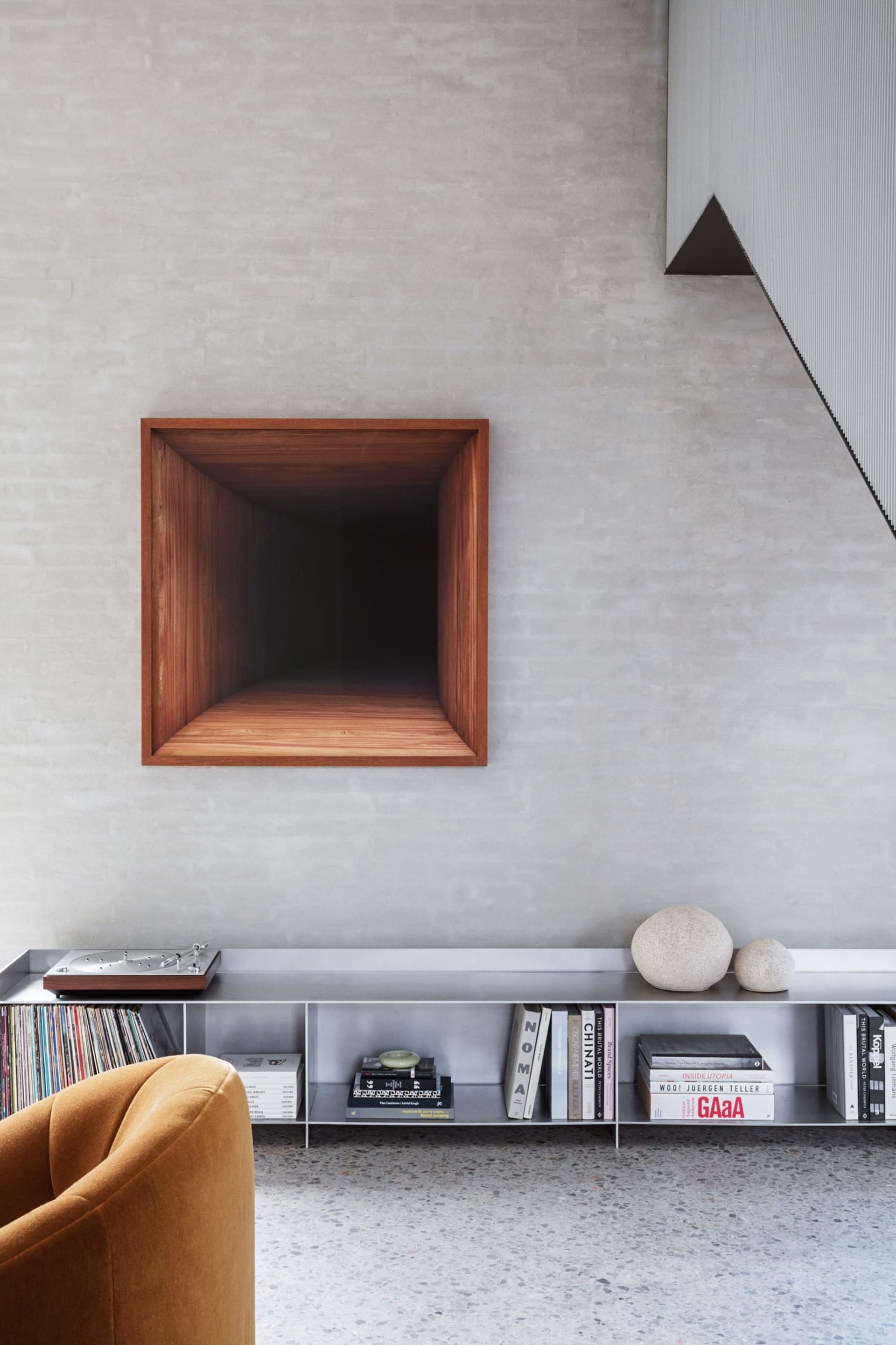 Modern minimalist living room featuring a concrete space with a dark wooden niche, a yellow armchair, and a shelf with books